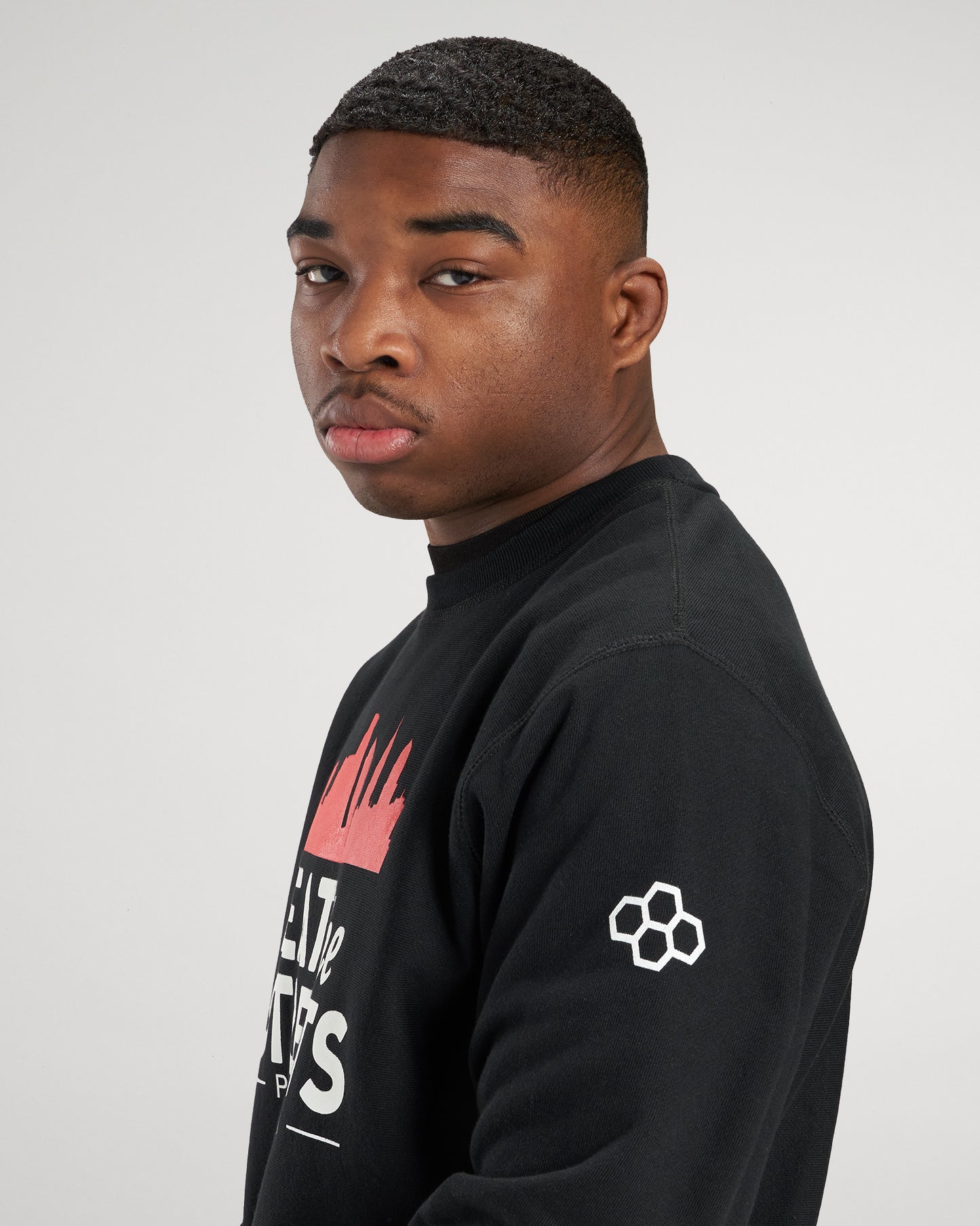 A young man with a confident expression poses in a black sweatshirt featuring a vibrant graphic design and a modern logo on the sleeve