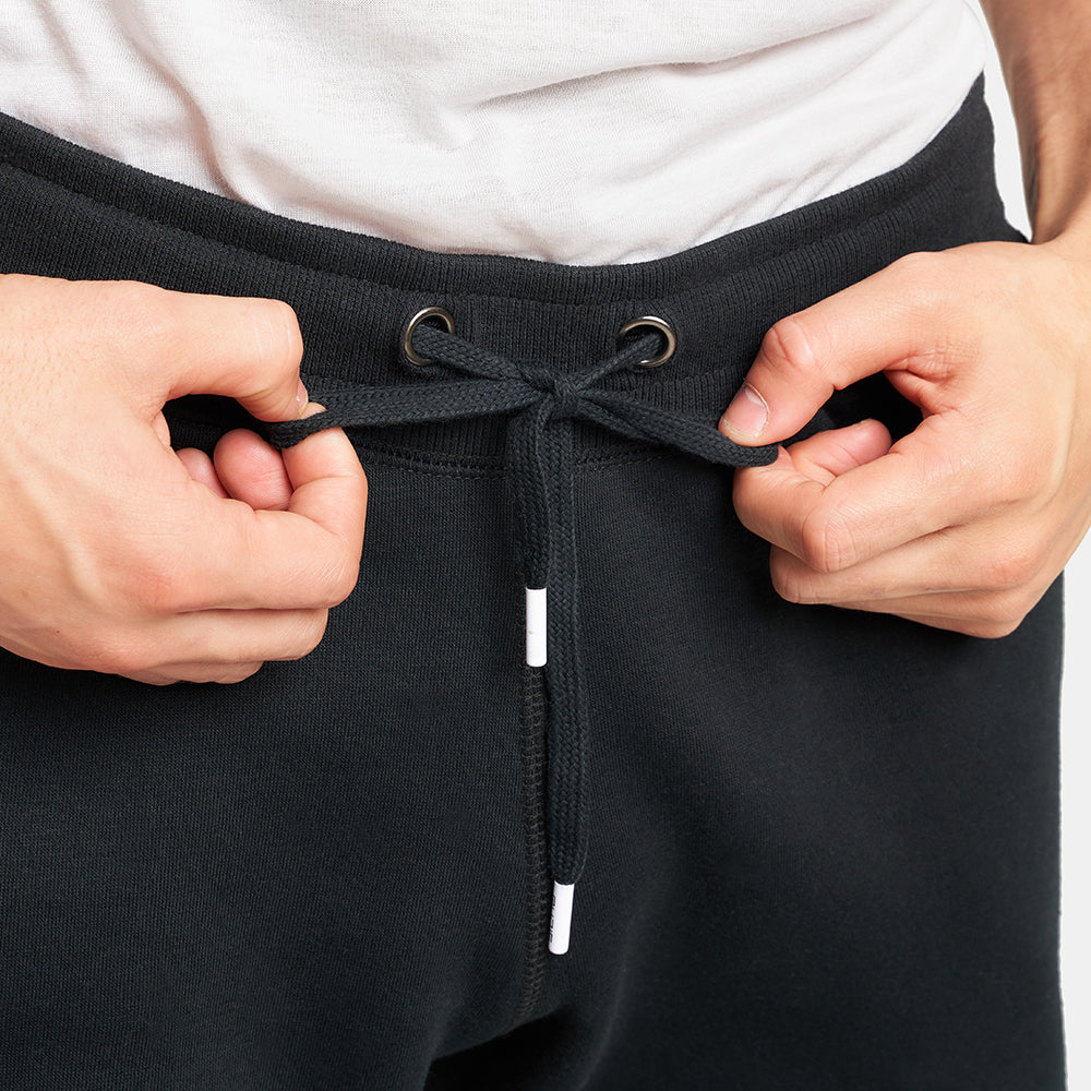 A close-up view of a person adjusting the drawstring of black sweatpants highlighting the textured waistband and eyelets