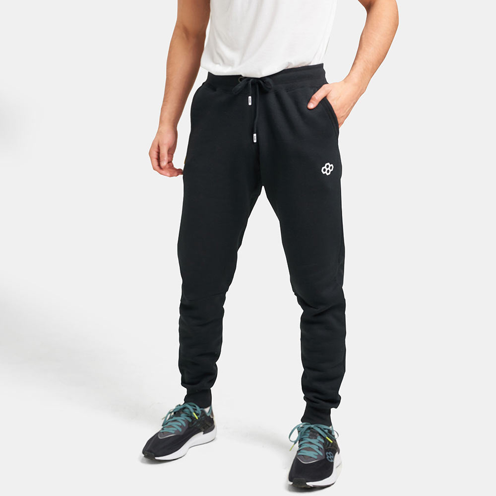 A man stands confidently in black sweatpants paired with a white t-shirt and stylish athletic shoes showcasing a casual and sporty look
