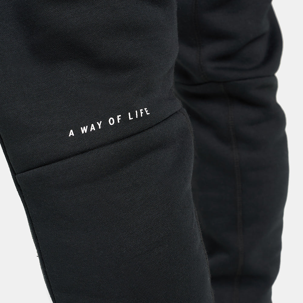 A close-up view of black sweatpants featuring the phrase A WAY OF LIFE printed in white on the thigh area
