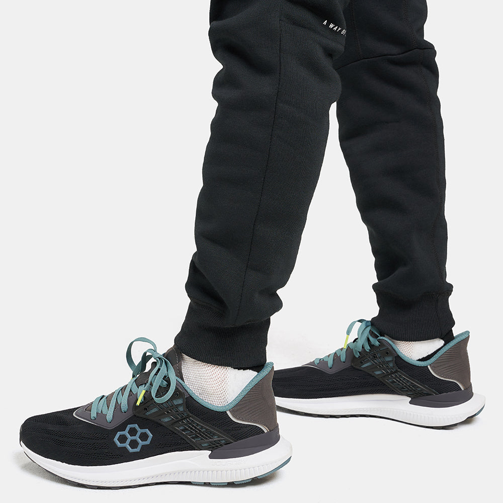 A close-up view of a person wearing sleek black athletic shoes with mint green accents paired with dark jogger pants