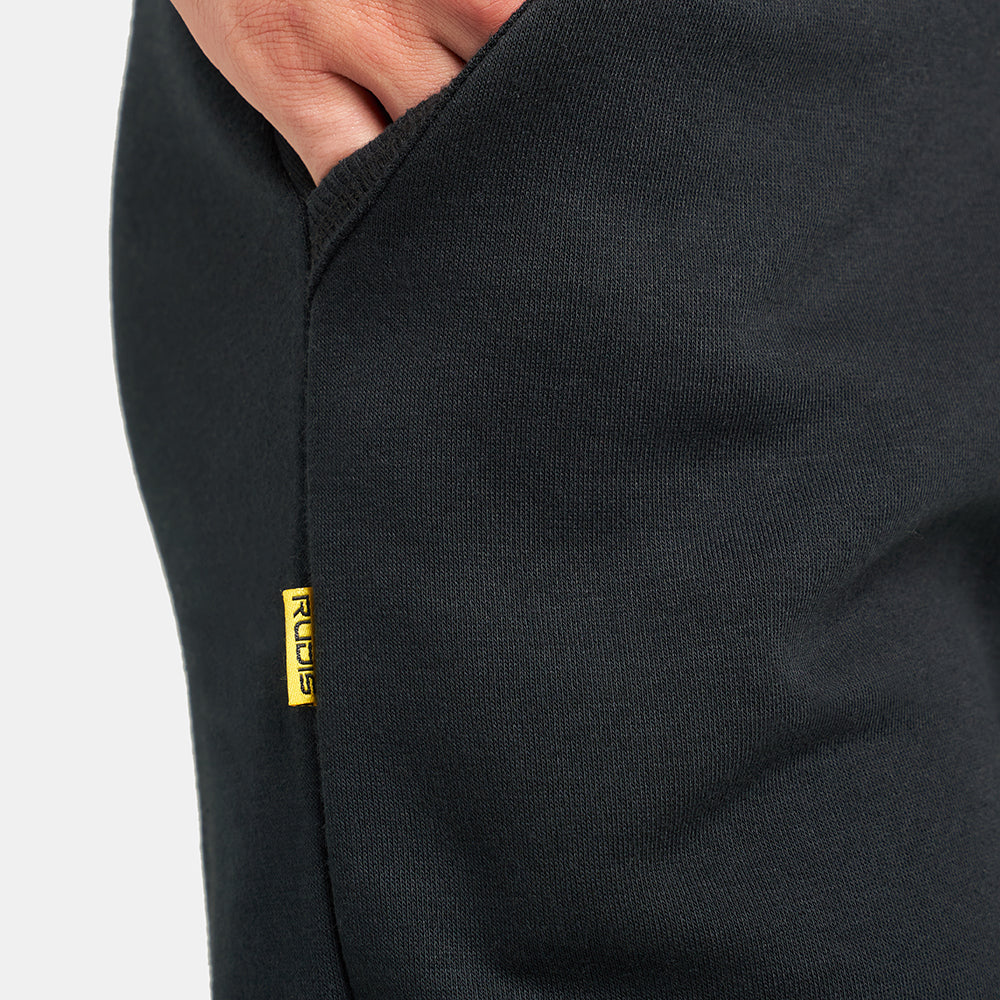 A detailed close-up of a black athletic pant pocket featuring a hand casually placed inside and a visible brand tag in yellow