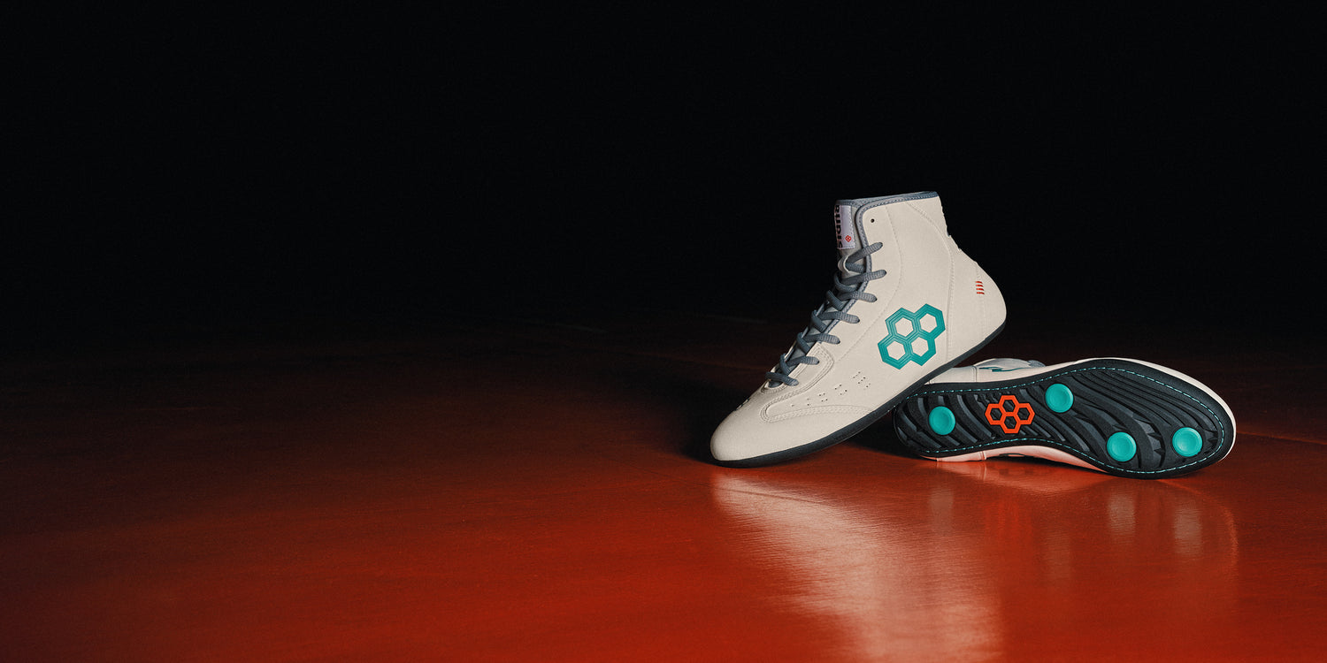 Banner image of the RUDIS International Wrestling Shoes - Utility (Cream shoes with cool green quadhex and grey accents) styled on an orange wrestling mat.