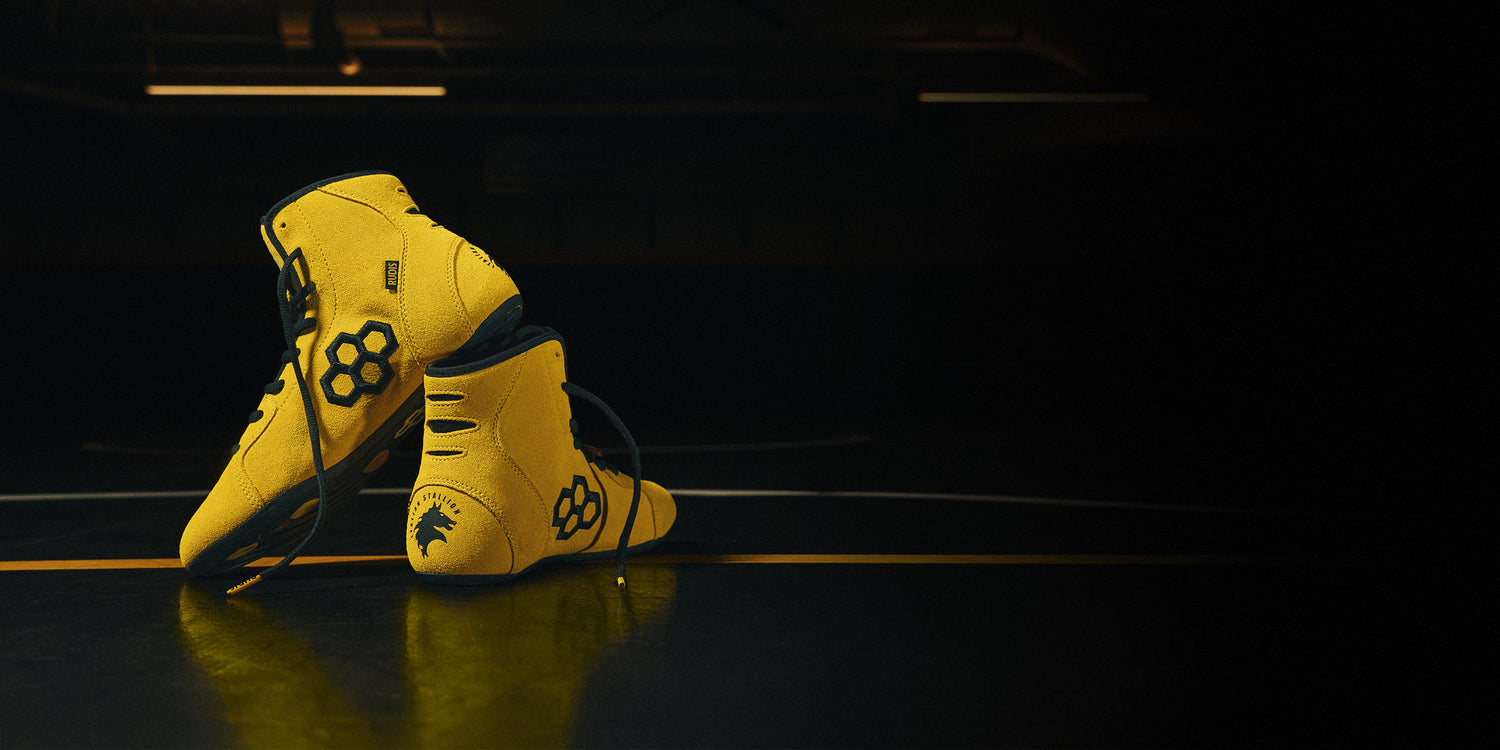 Banner image of the yellow ROCKY x RUDIS International Wrestling Shoes sitting on a black wrestling mat.