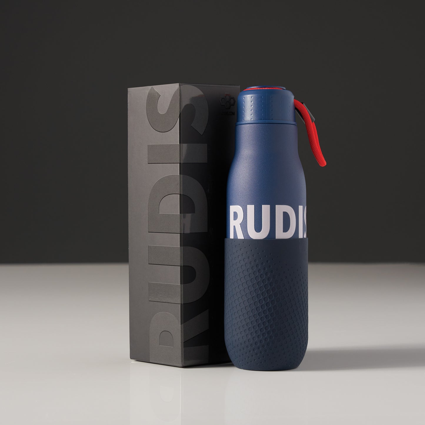 A modern insulated water bottle in navy blue accompanied by its sleek black packaging featuring the brand name RUDIS prominently displayed
