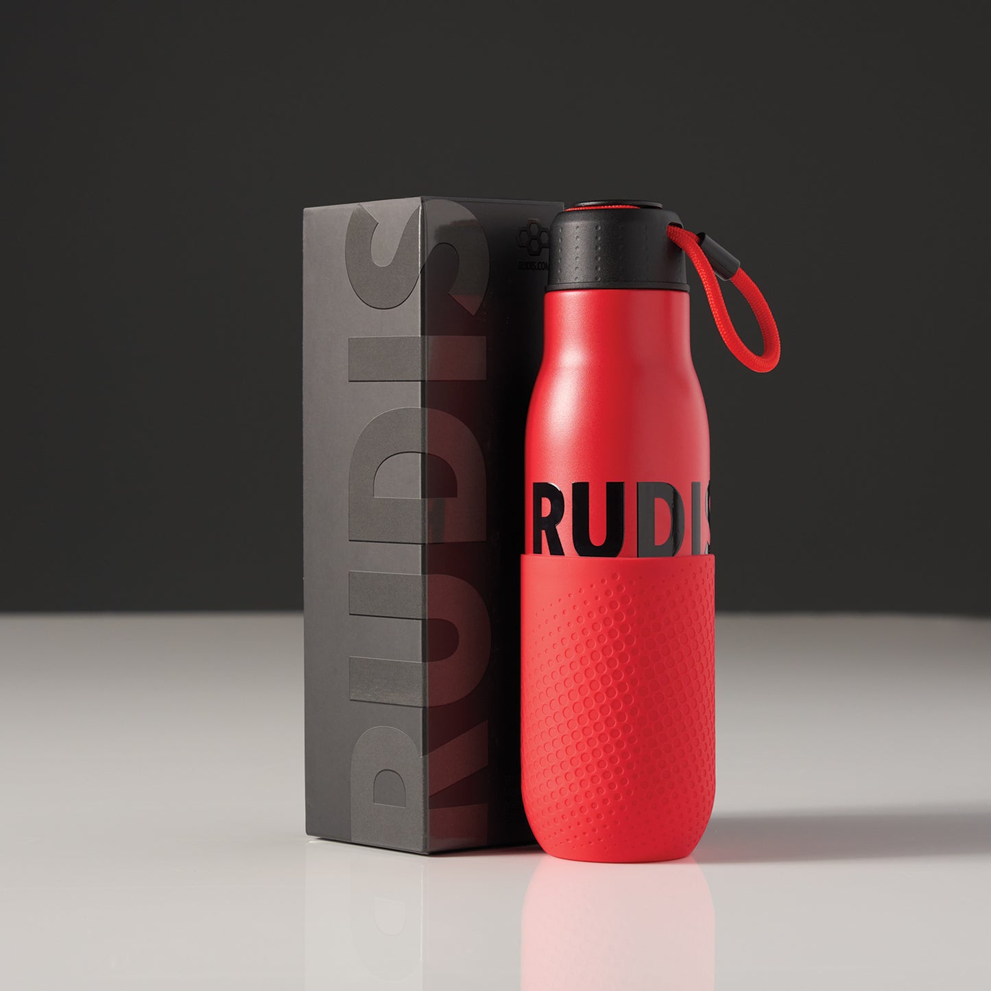 This image features a vibrant red water bottle with a black lid displaying the brand name RUDIS prominently on its body and accompanied by a sleek black packaging box