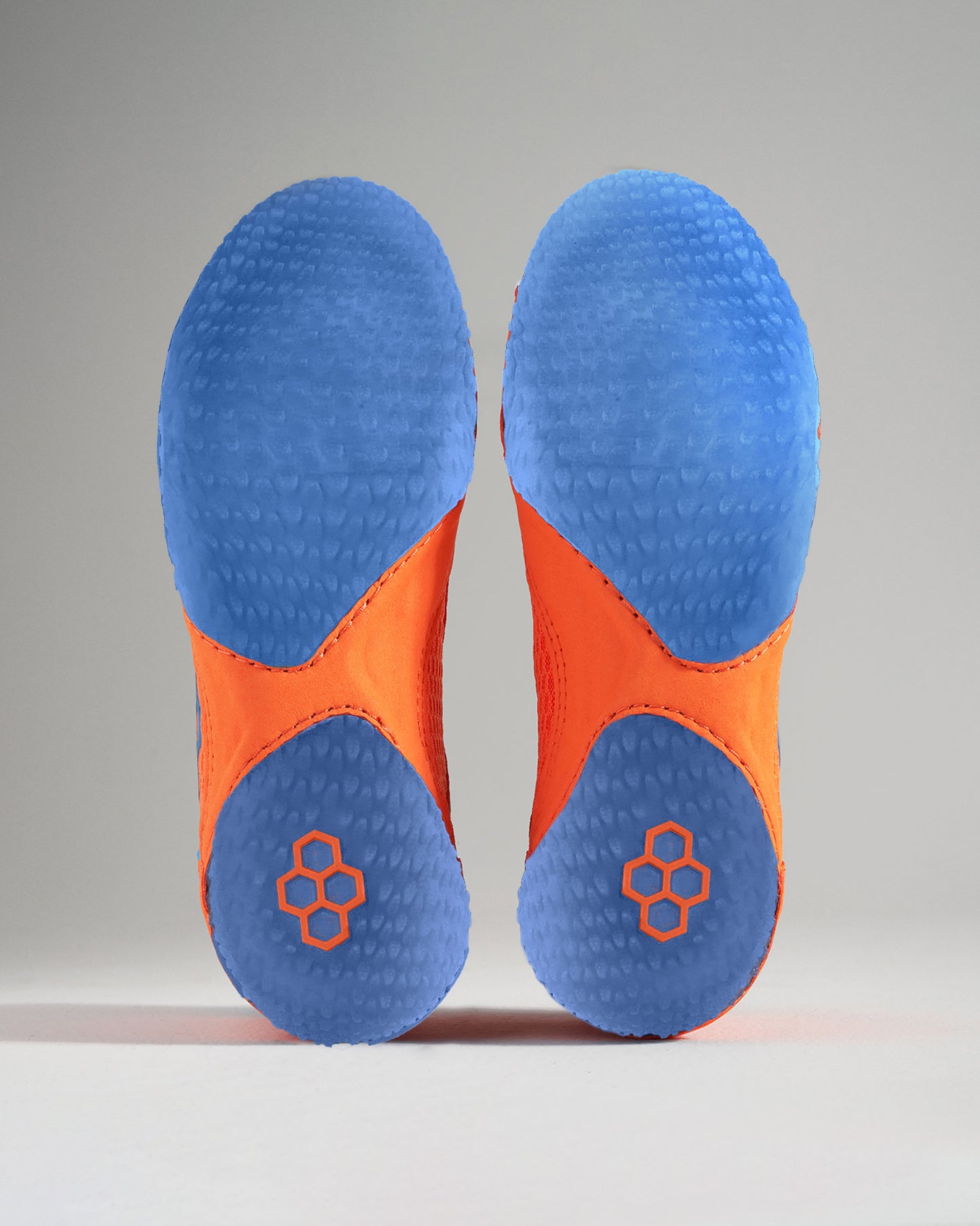 A close-up view of a unique pair of athletic shoes showcasing an orange upper and a blue textured sole designed for performance and style