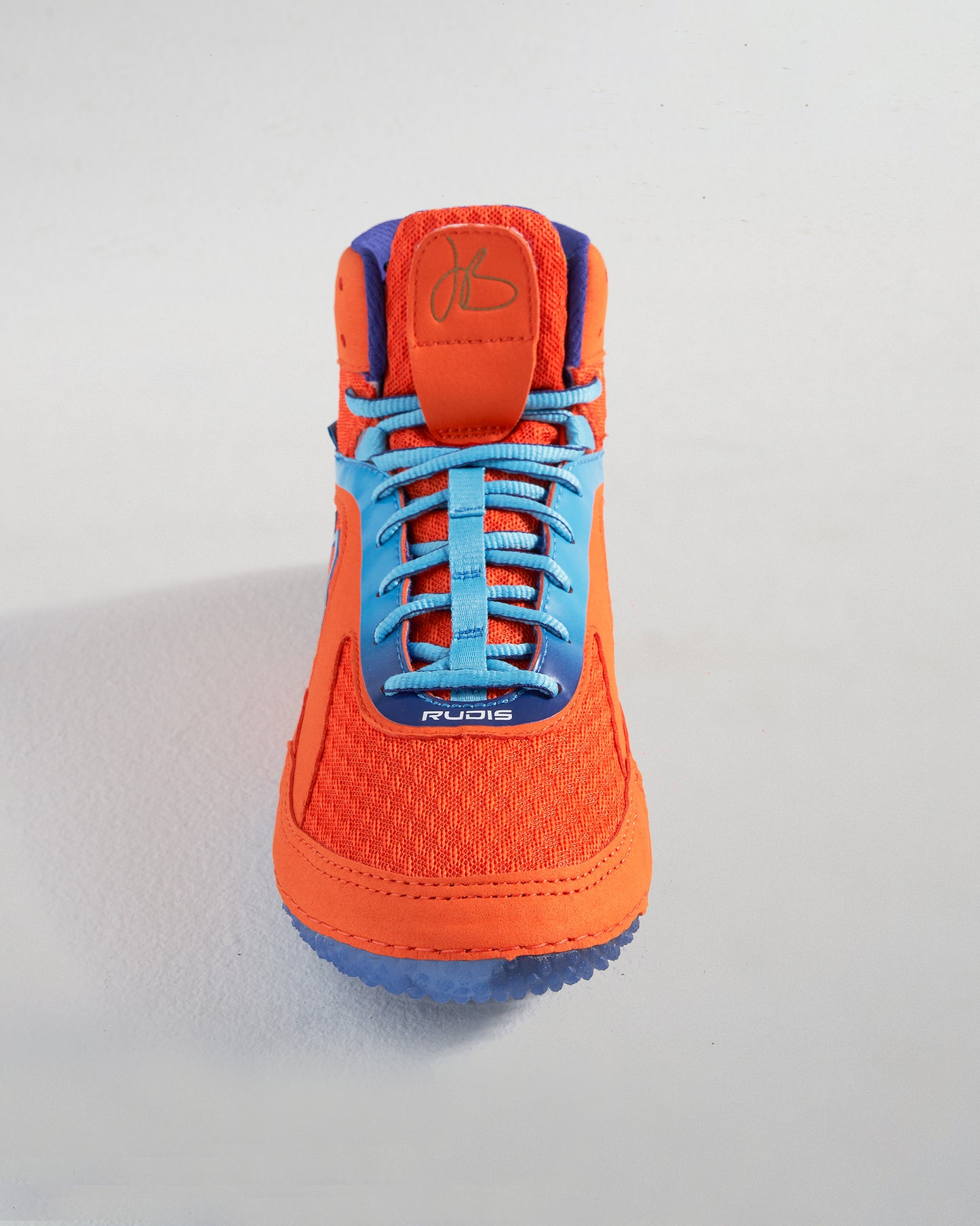 A vibrant orange wrestling shoe with blue laces designed for high performance and style featuring a unique textured sole and the word RUDIS prominently displayed