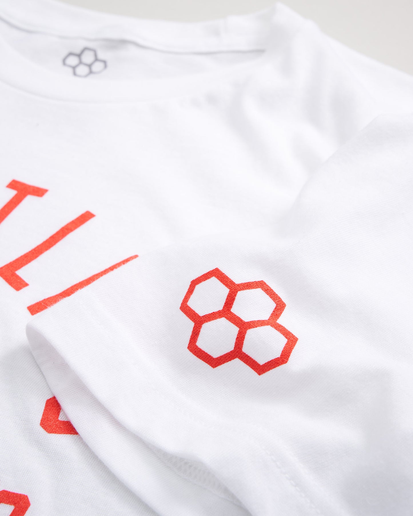 A close-up of a white t-shirt featuring bold red lettering and a geometric logo on the sleeve