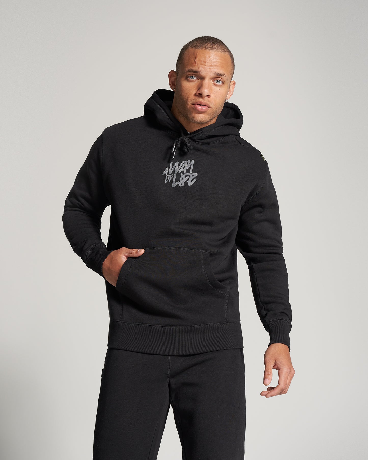 A man wearing a black hoodie with a bold graphic logo showcasing a confident expression against a light background