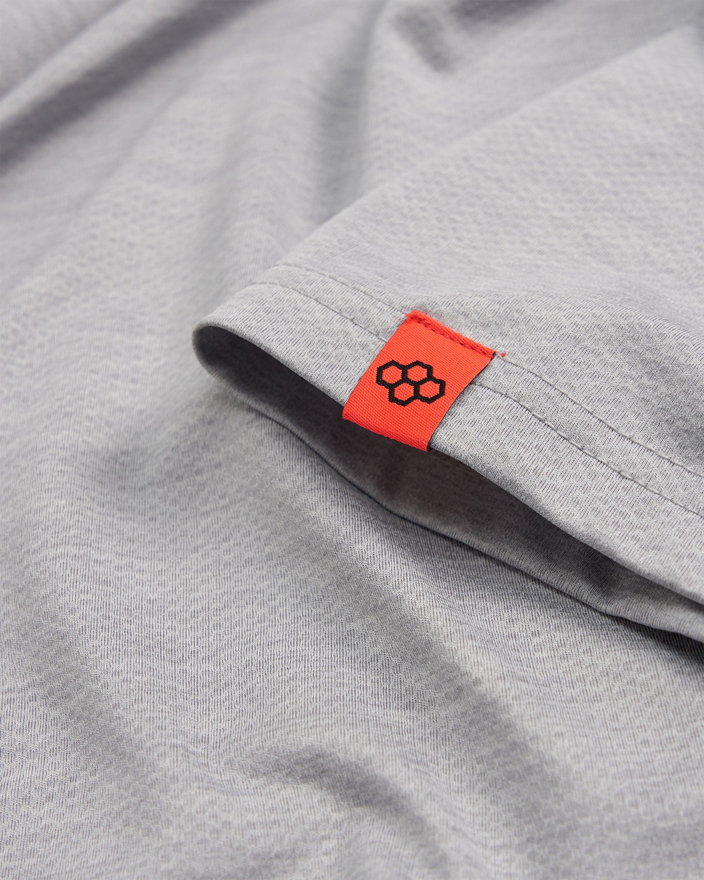 A close-up of a light gray fabric with an orange tag featuring a logo showcasing its texture and stitching details