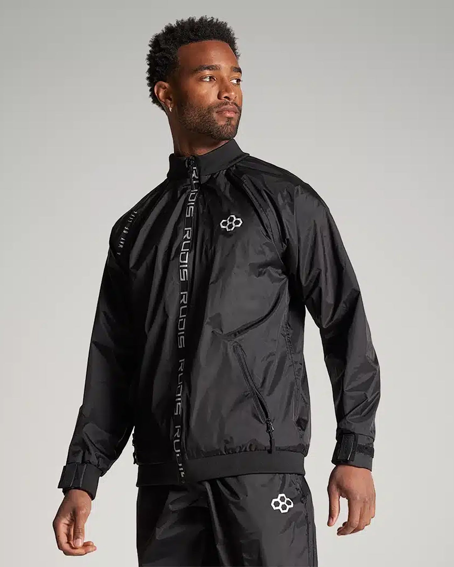 A man wearing a stylish black athletic jacket with a zippered front and matching pants showcasing a modern design ideal for sporty fashion