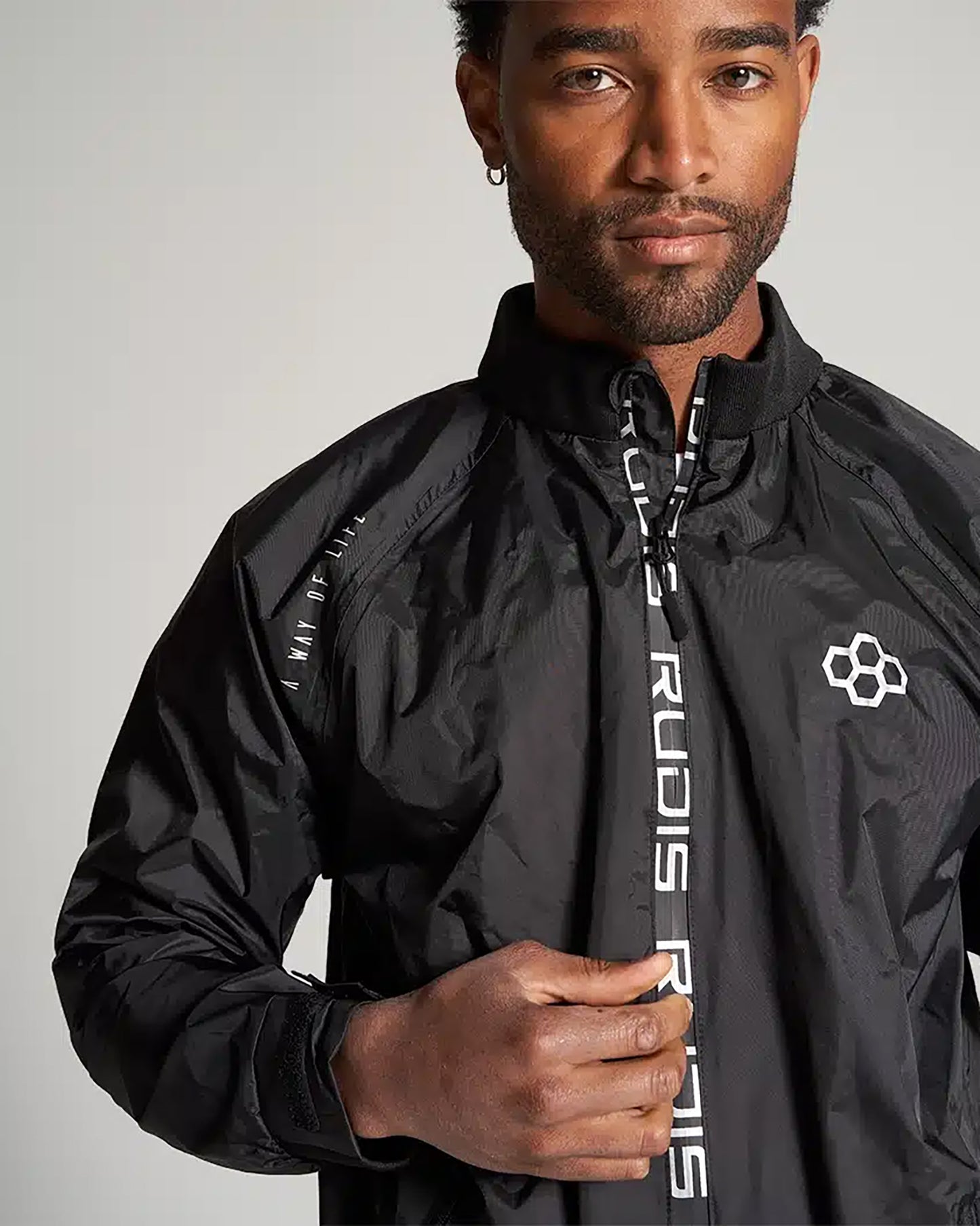 A close-up portrait of a man wearing a sleek black jacket featuring the RUDIS logo showcasing modern athletic style and a confident expression