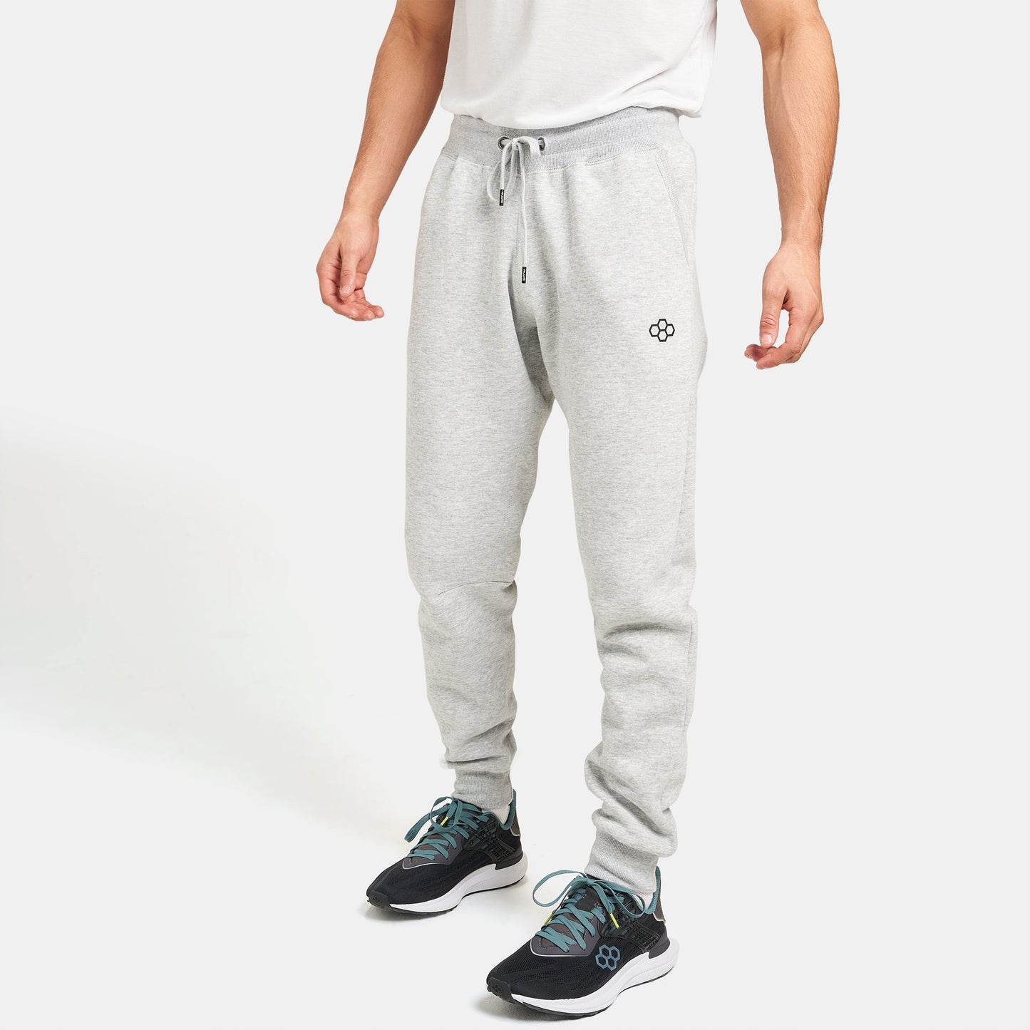 A man stands in a casual outfit featuring light gray sweatpants and black athletic shoes with teal accents