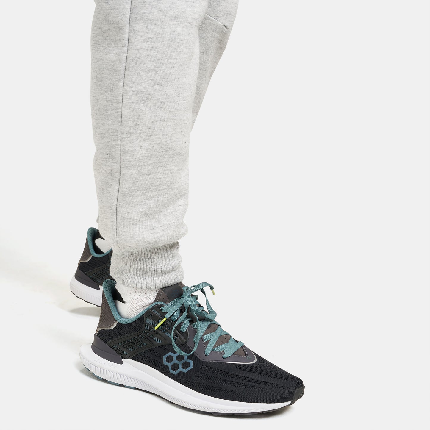 A close-up view of a persons foot wearing a modern black athletic shoe with teal accents paired with gray sweatpants