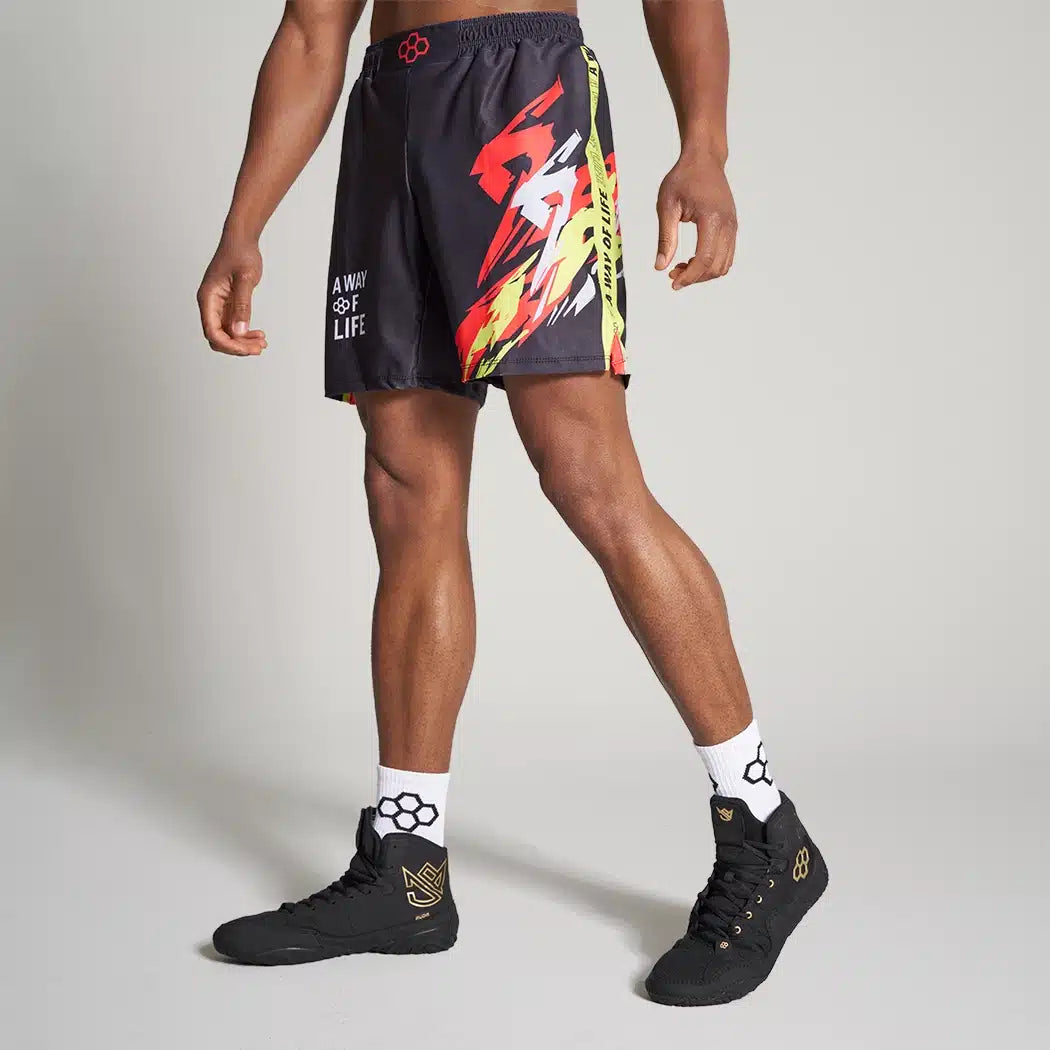 A male model showcases vibrant black athletic shorts with striking red and yellow graphics complemented by black sneakers and patterned socks