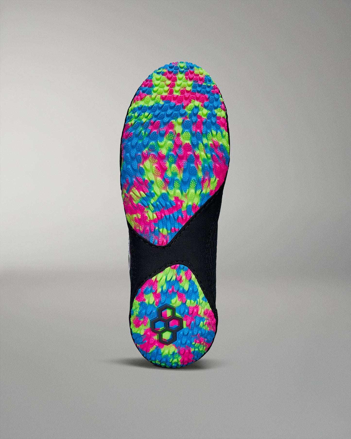 The shoe sole exhibits a colorful textured design with pink, blue, and green patterns for enhanced grip, against a black background and subtle gray surroundings.