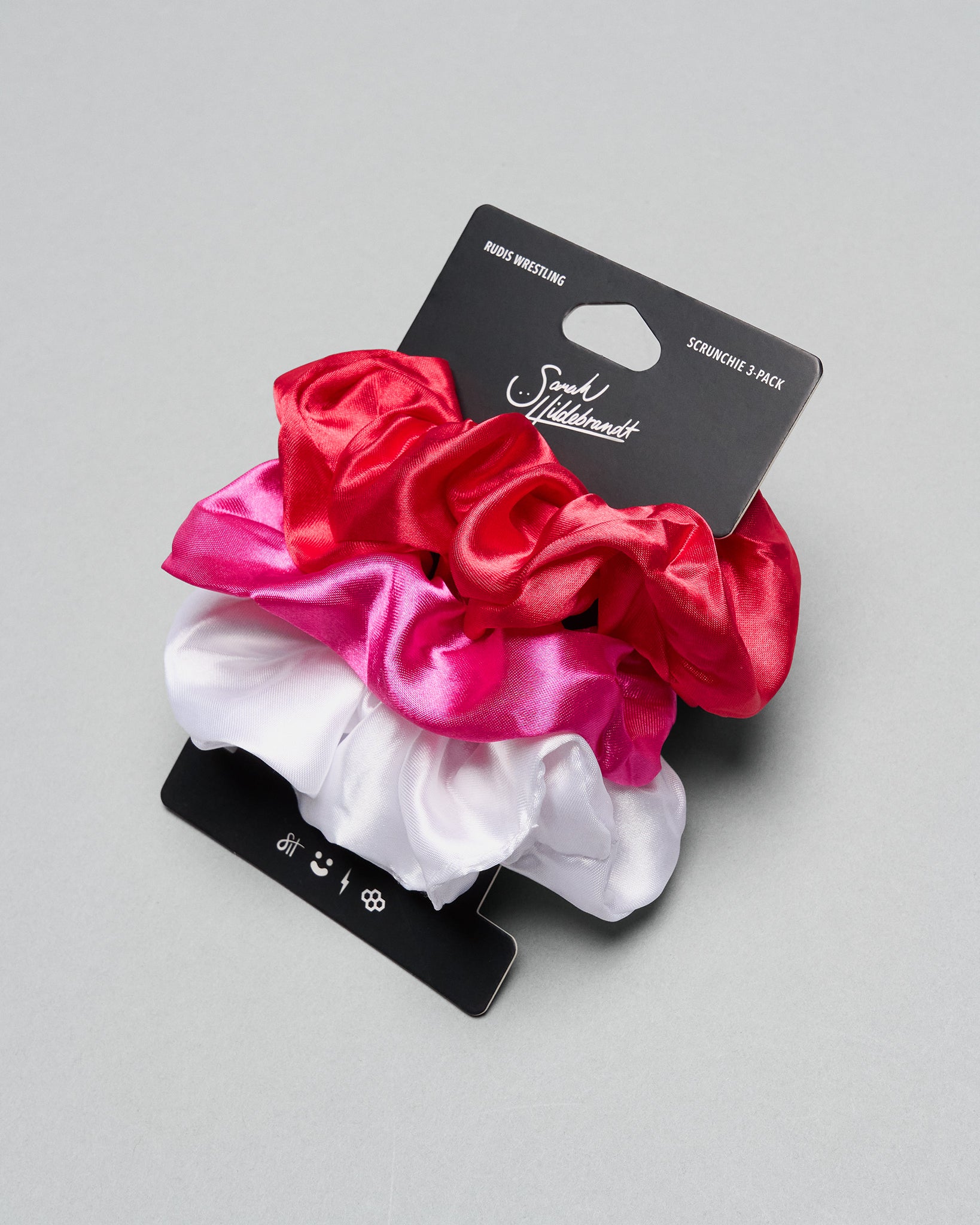 Set of three satin scrunchies in red, pink, and white on a gray background with a brand label.