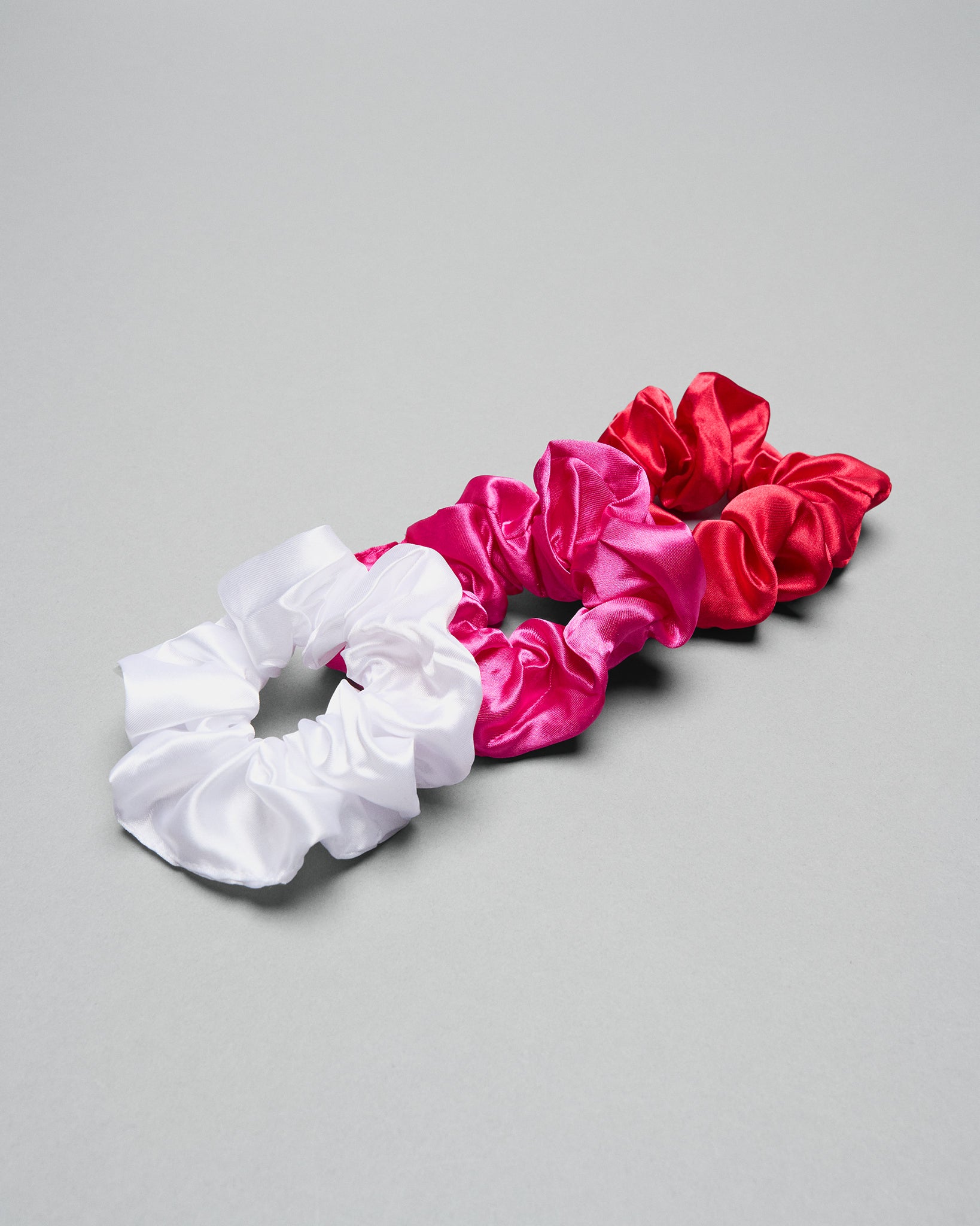 Set of three scrunchies in white, pink, and red on a gray background