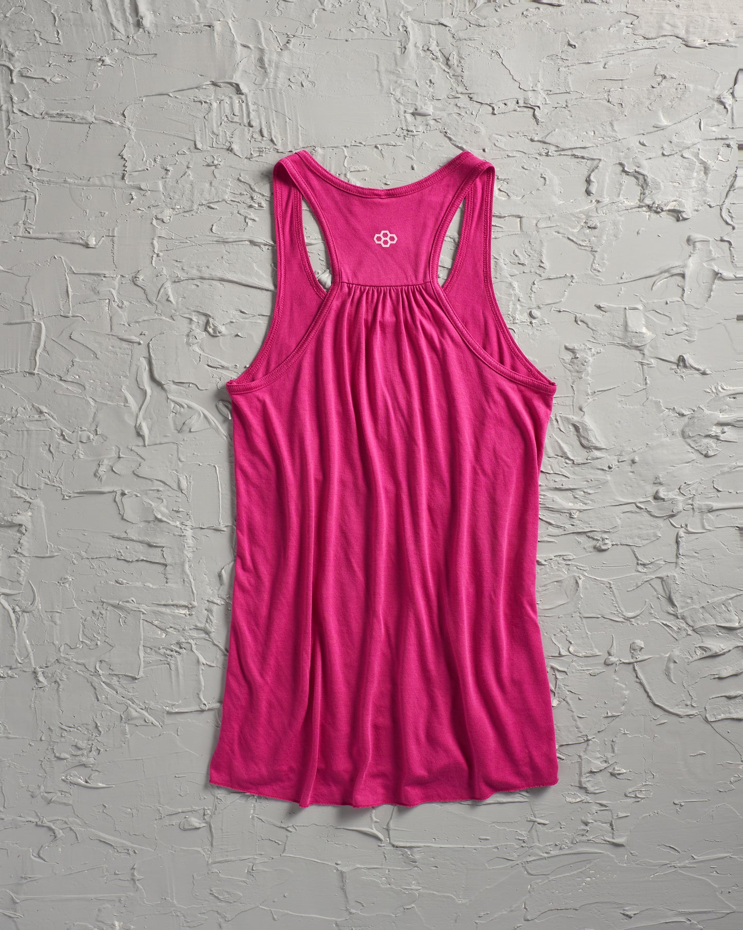 A vibrant pink tank top displayed against a textured gray background designed with a racerback cut and a decorative logo at the back