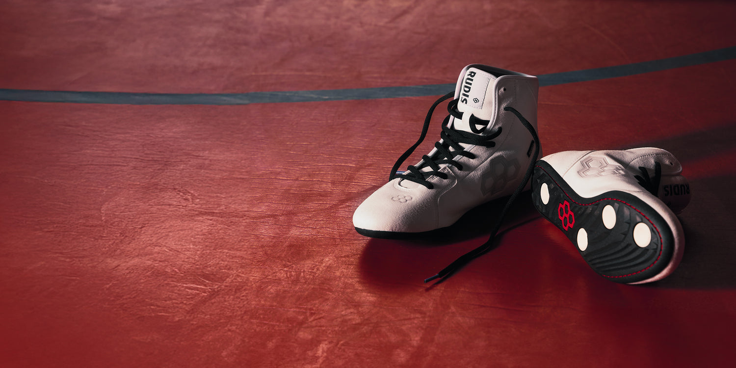 Banner image of the RUDIS International Wrestling Shoes - White sitting on a red wrestling mat.