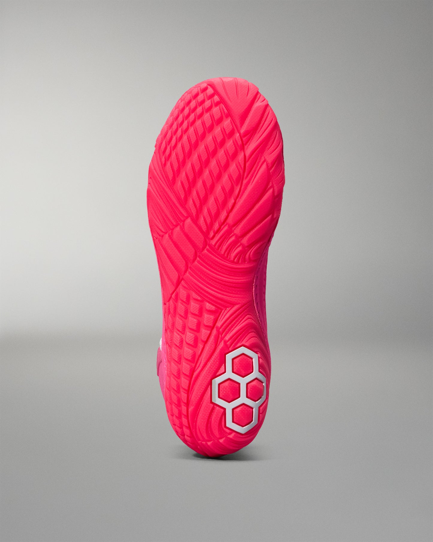 Close-up of a pink wrestling shoe sole with a hexagonal pattern on a gray background