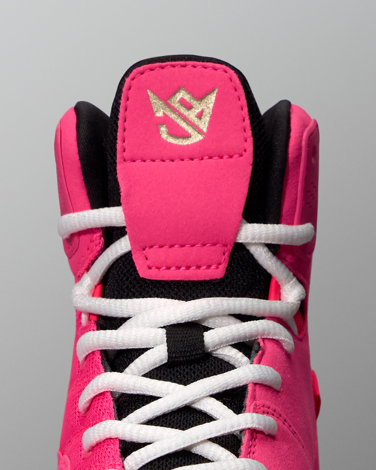 Close-up of a pink and black wrestling shoe with white laces on a gray background