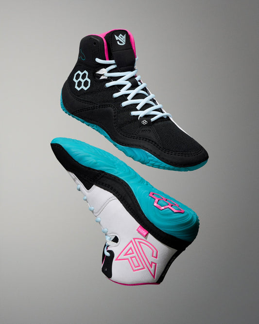 Pair of black, white, and teal wrestling shoe with pink accents on a gray background