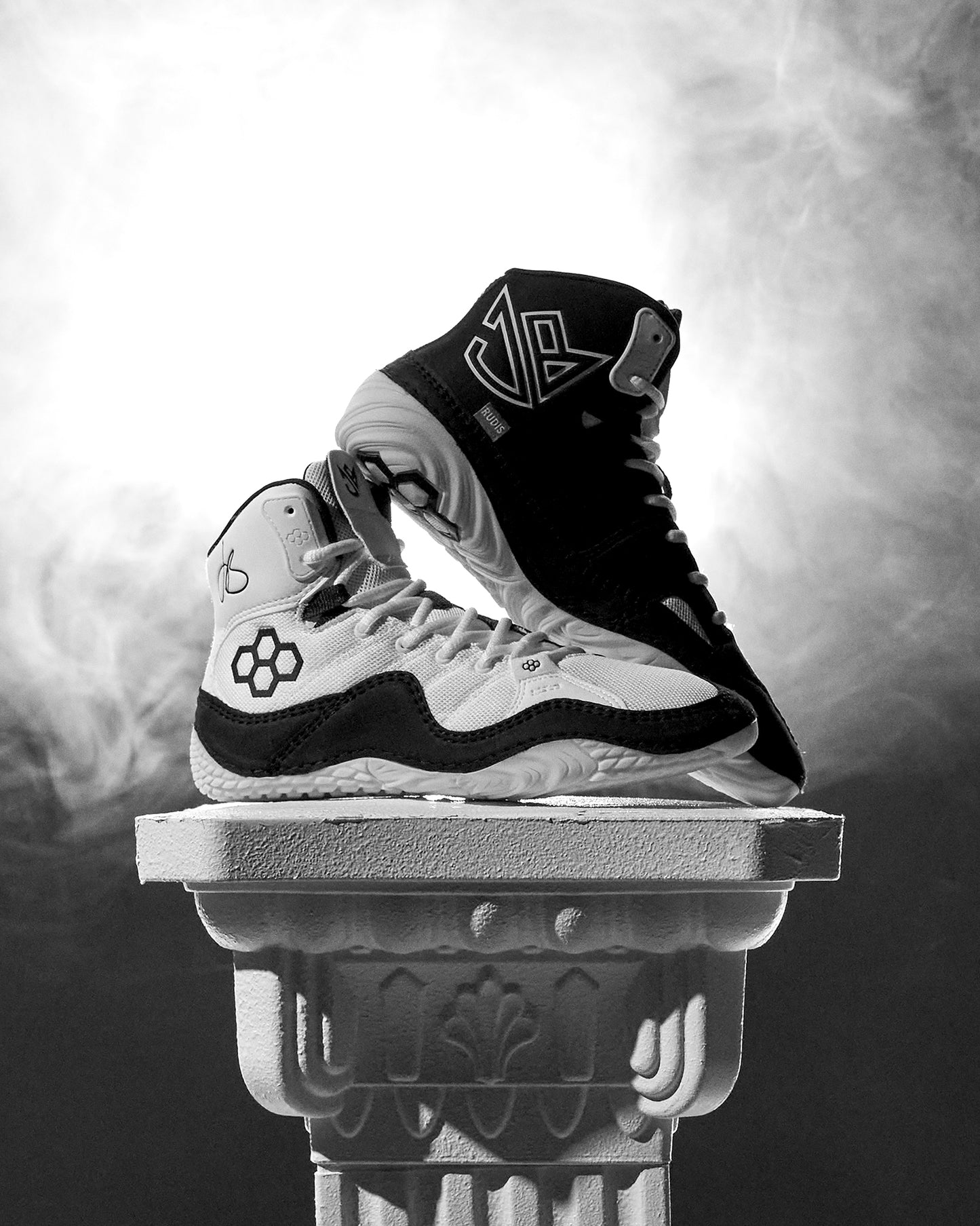 Black and white Jordan Burroughs Wrestling shoes on a decorative pedestal with a smoky background