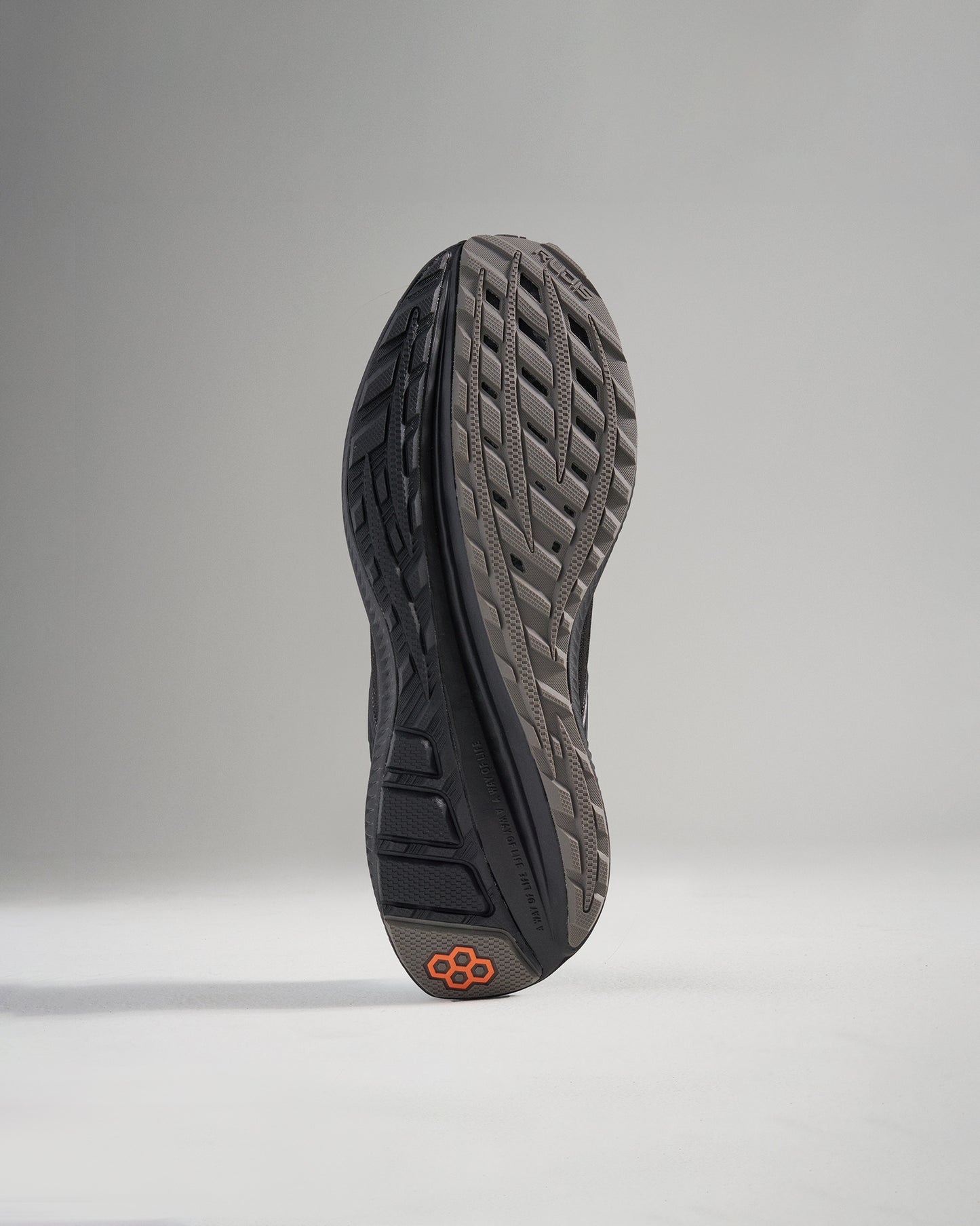 The image displays the sole of a modern athletic shoe featuring a unique tread pattern and a striking orange accent