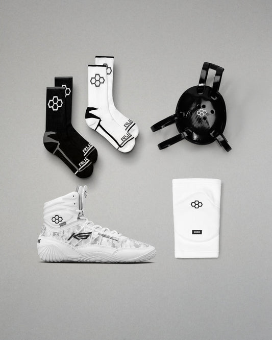 White wrestling shoes, black and white socks, and a black headgear on a gray background