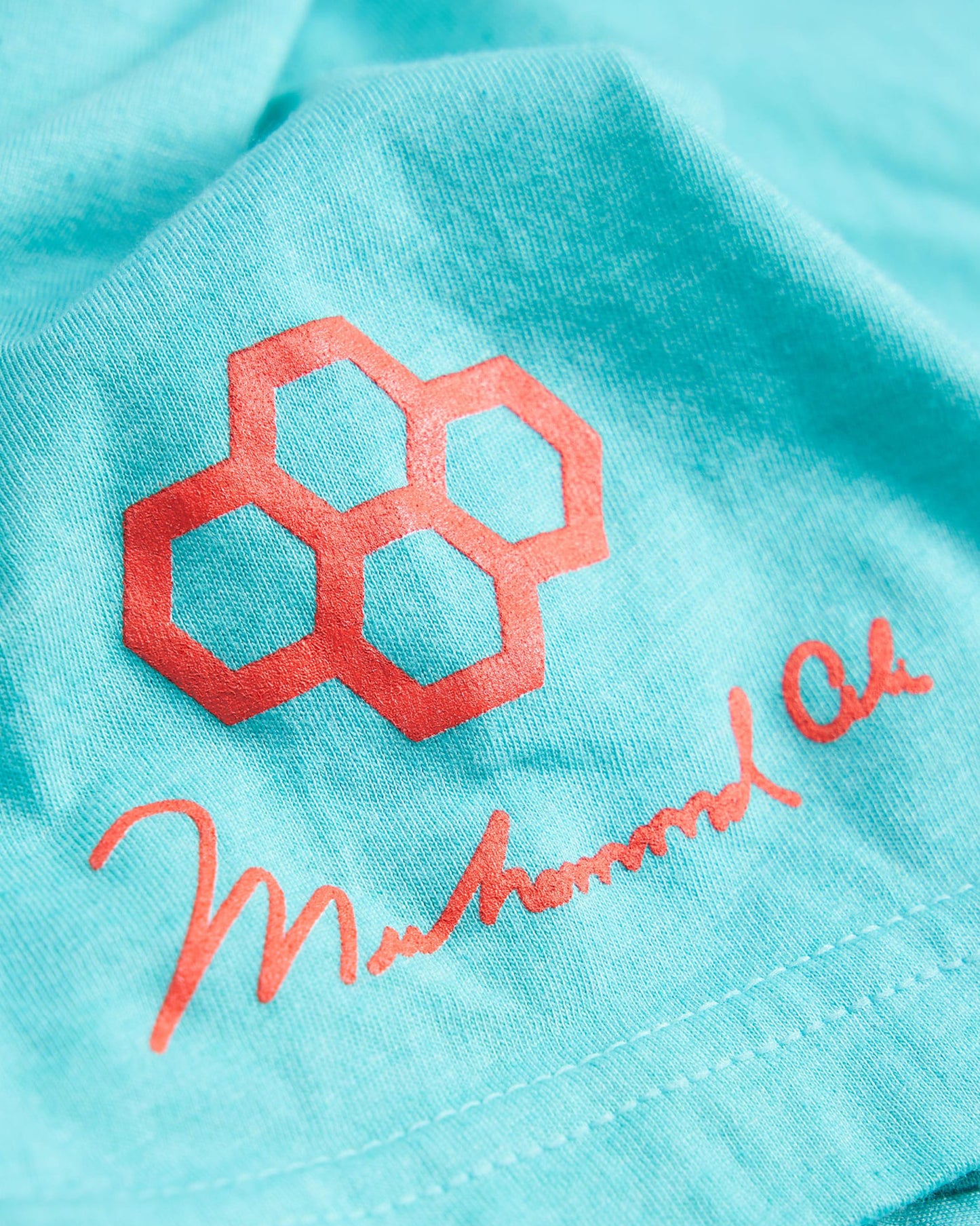 A close-up view of a turquoise fabric featuring a vibrant red hexagonal logo and the signature of Muhammad Ali