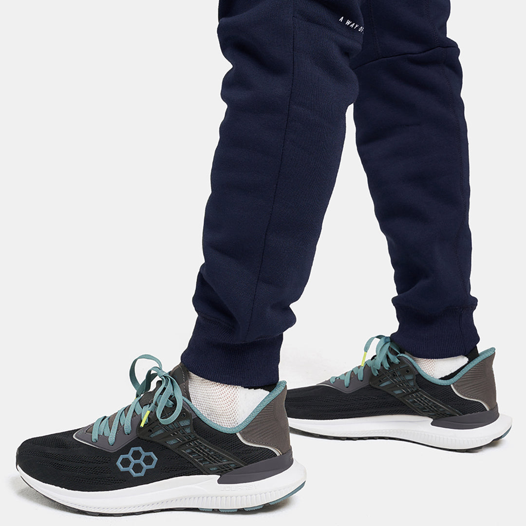 A person wearing dark navy sweatpants and modern black and gray running shoes with light blue accents captured in a casual stance on a light background