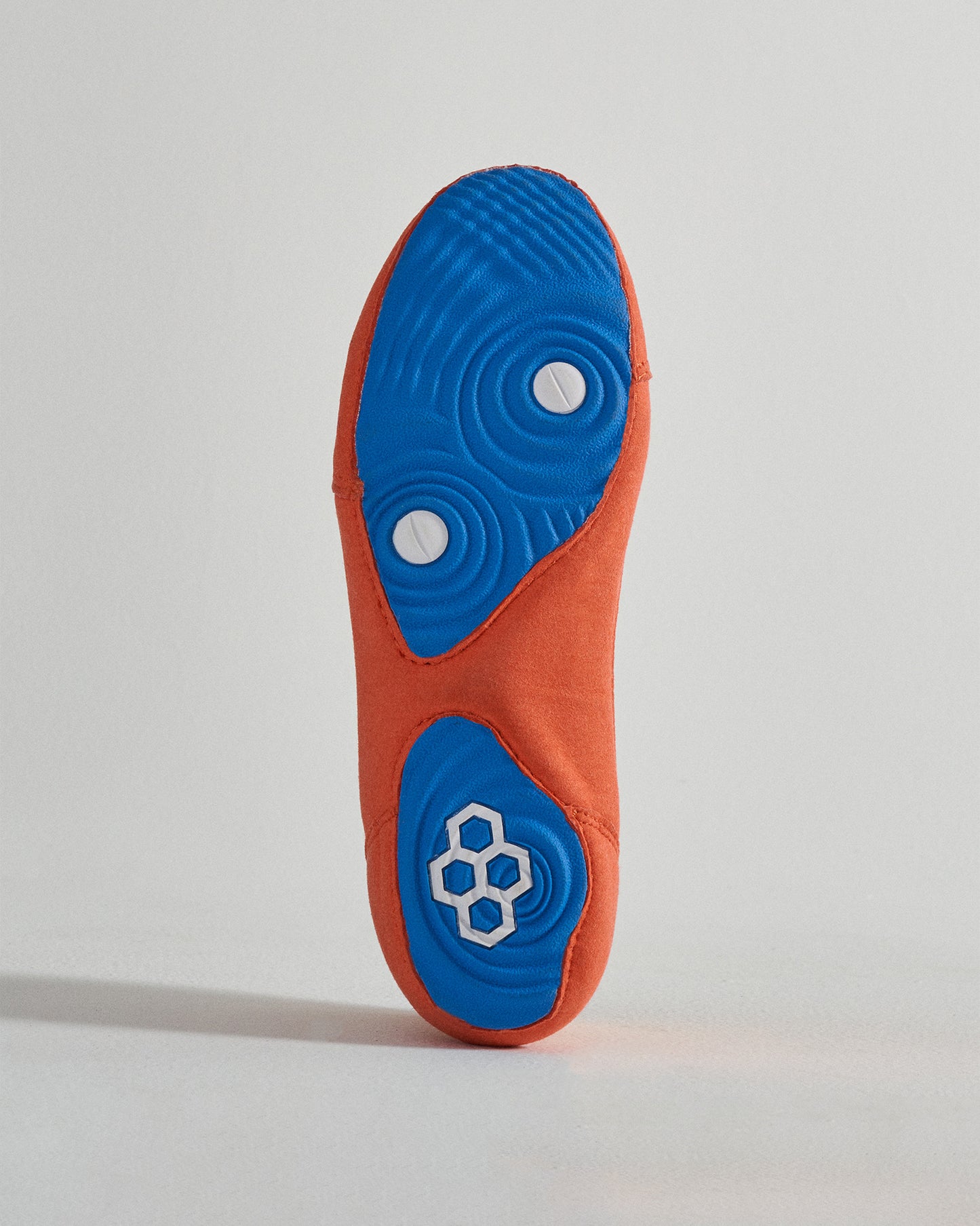 This image displays the sole of an orange athletic shoe with a textured blue outsole featuring circular grips and a white logo on the side