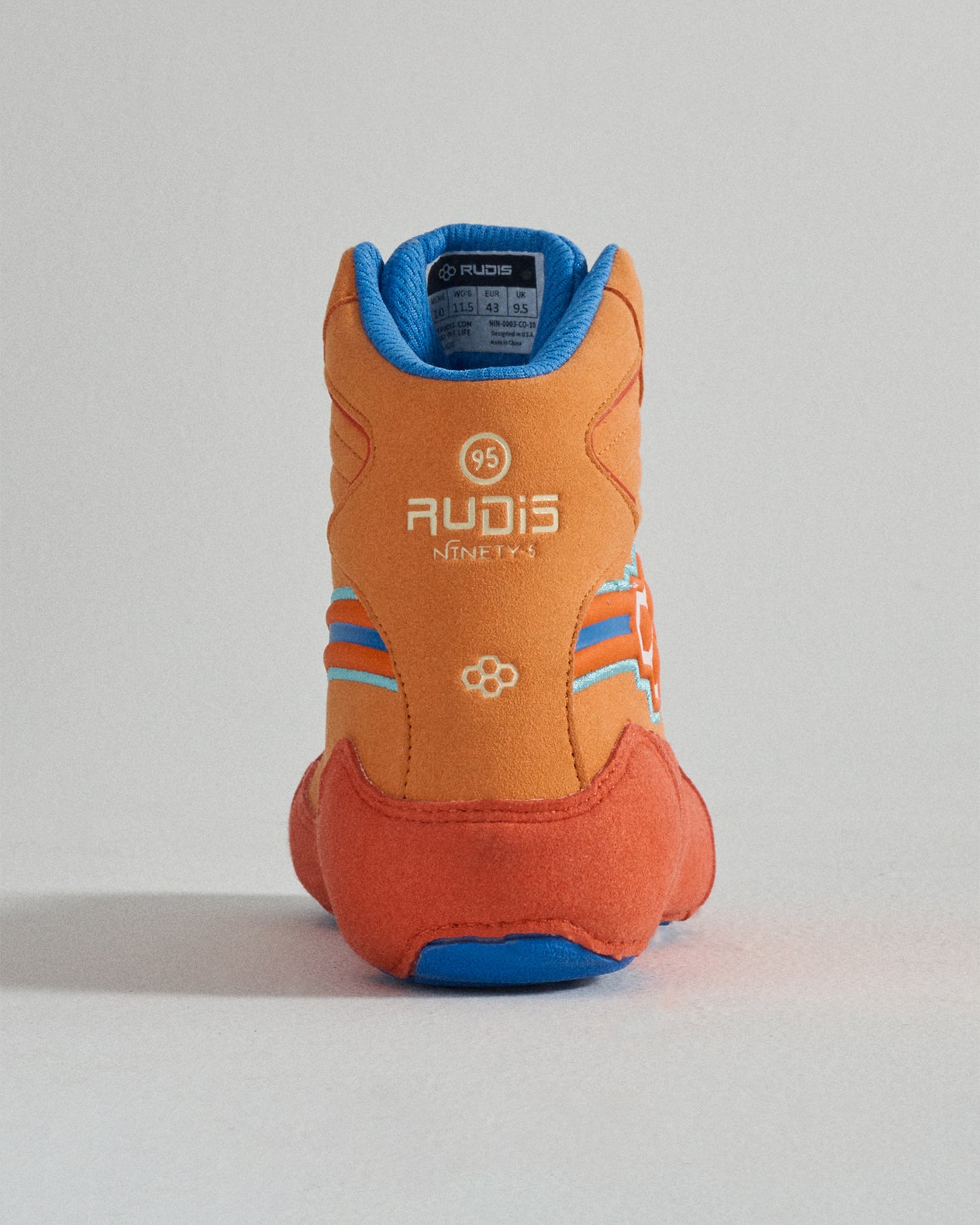 A vibrant orange wrestling shoe with blue accents and the logo RUDIS prominently displayed at the back