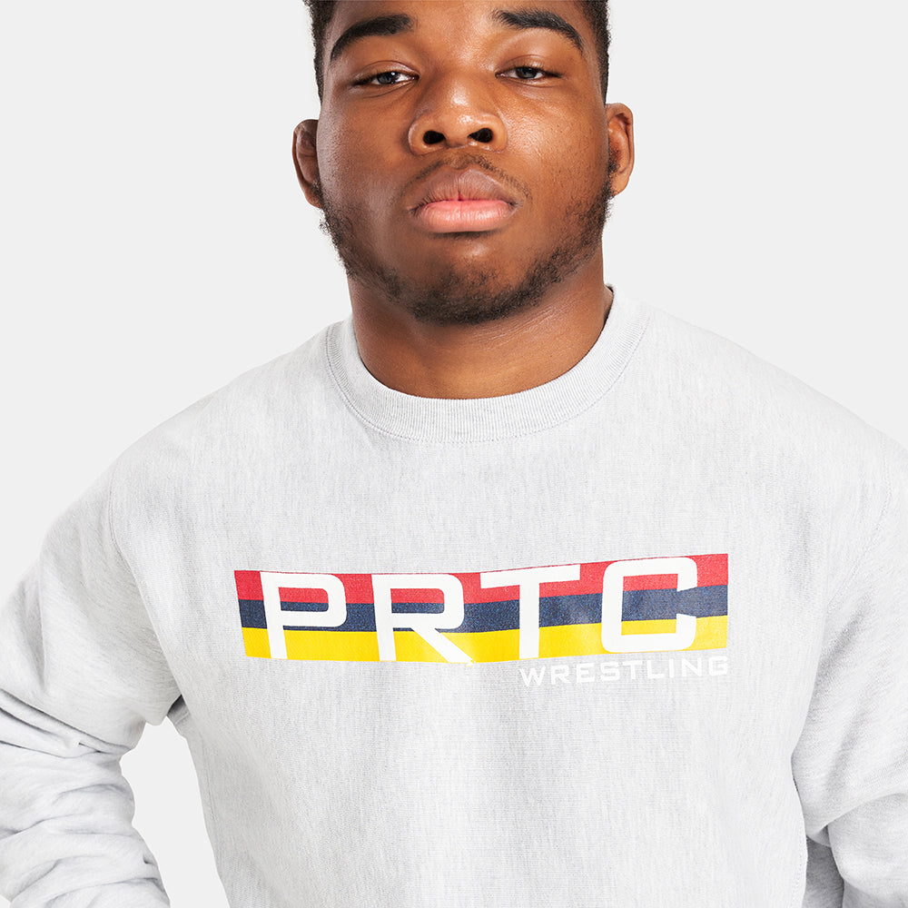 A young man in a gray sweatshirt featuring bold red blue and yellow stripes and the text PRTC WRESTLING