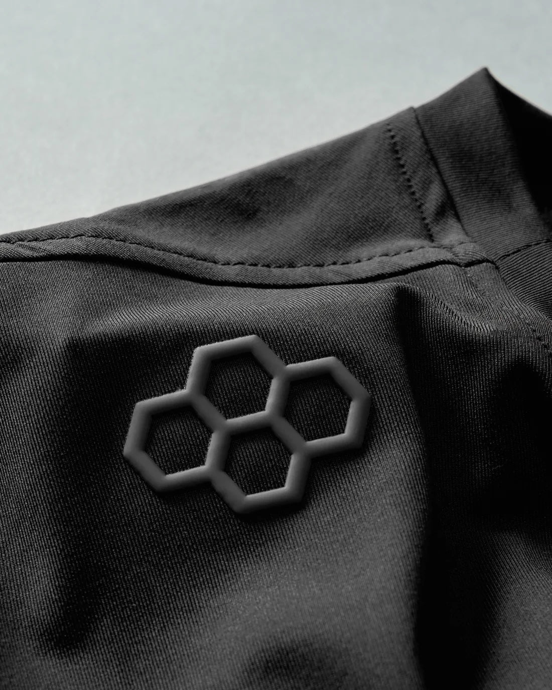 A close-up view of black fabric with a textured hexagonal logo, showcasing a modern and minimalist design suitable for activewear.