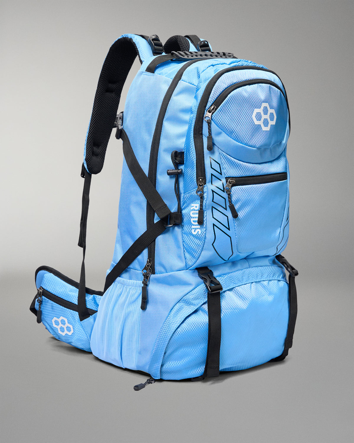 A light blue and black technical backpack shown from a three-quarters angle on a neutral gray studio background. The brand name 'RUDIS' is printed vertically on the front pocket, and a white geometric logo is visible on the front and hip belt.