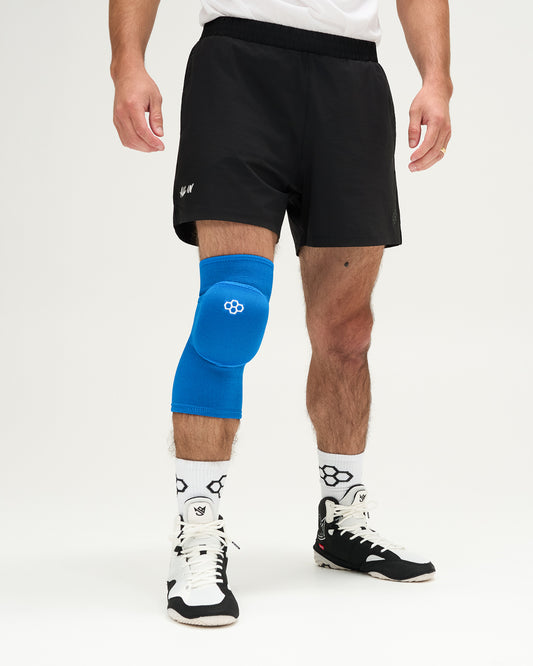 Person wearing blue knee pads and white athletic shoes on a plain background