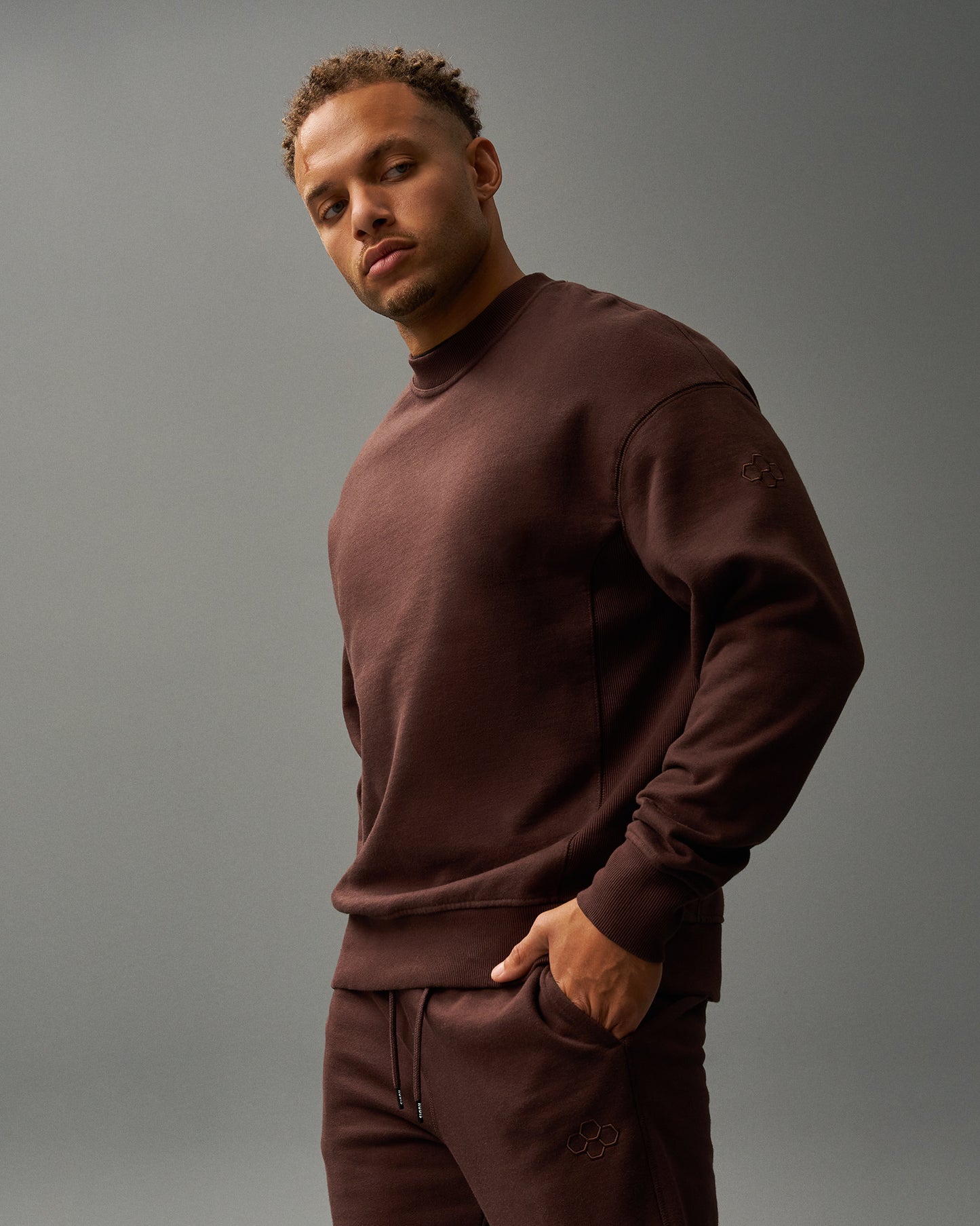 Man wearing a brown sweatshirt and pants against a gray background