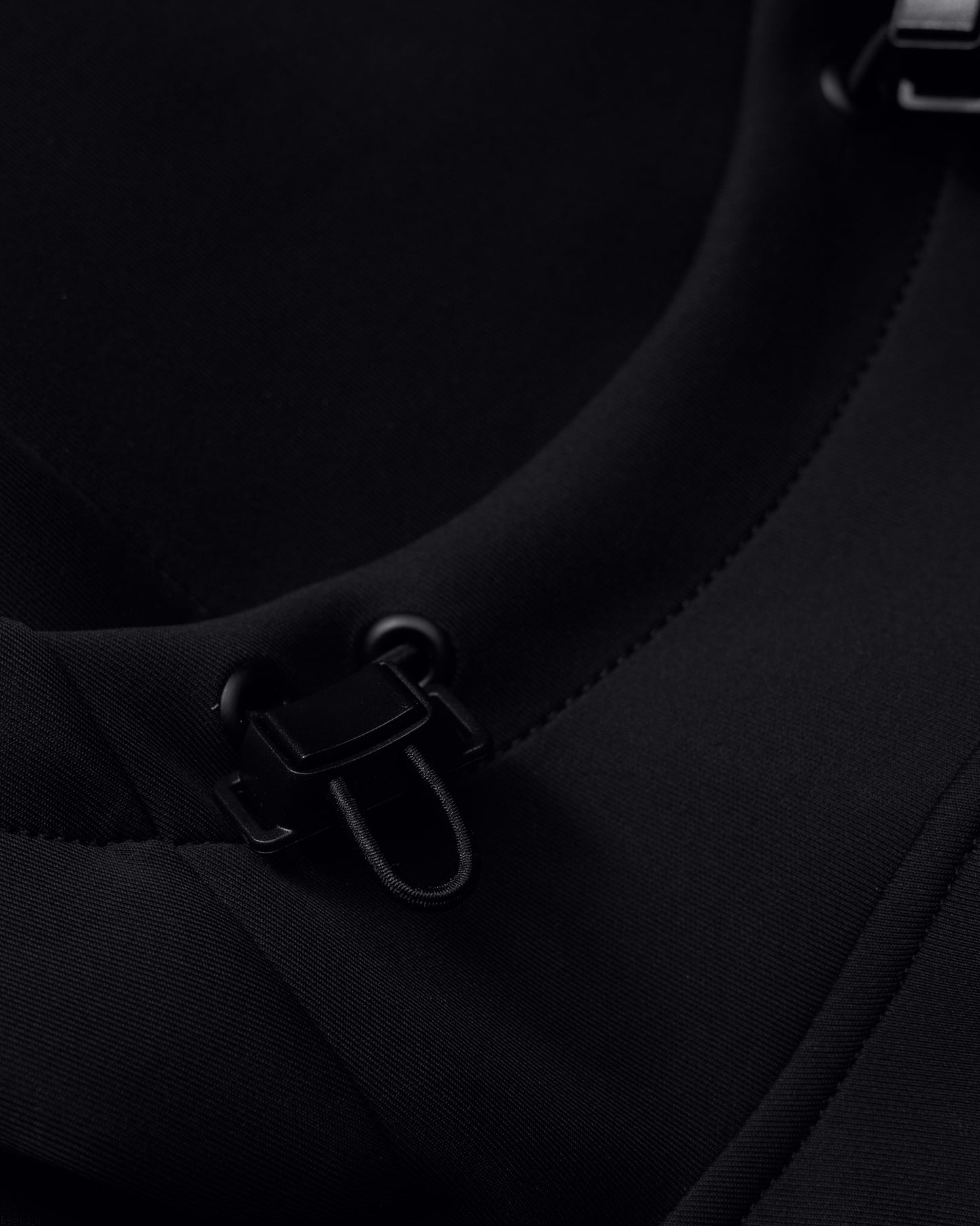 Close-up view of a black fabric featuring fastening elements and detailed stitching, showcasing practical design for active wear.