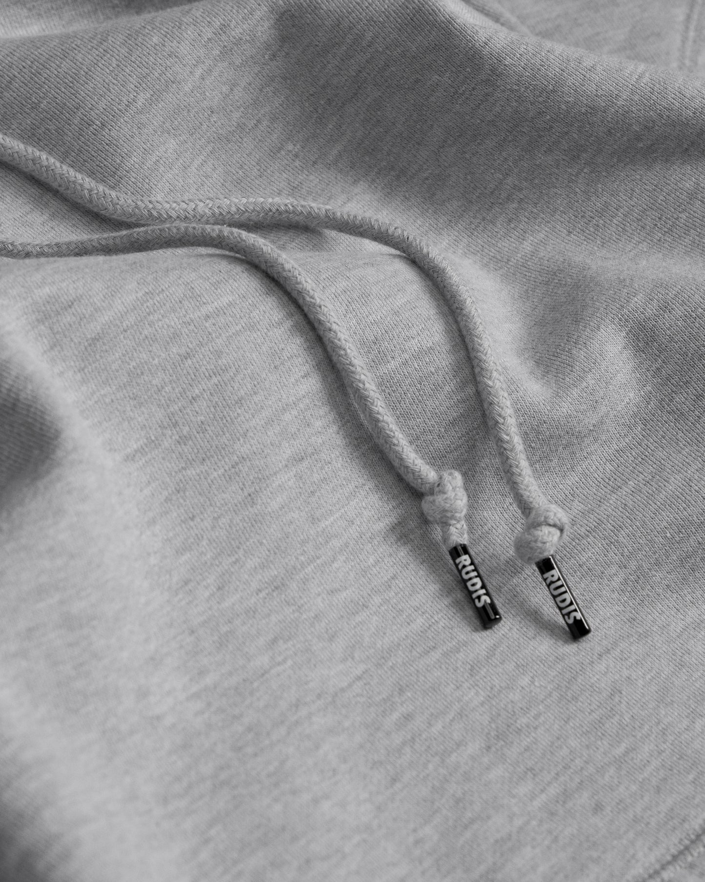 Close-up of gray hoodie with drawstring and 'RUDIS' brand logo on the aglet