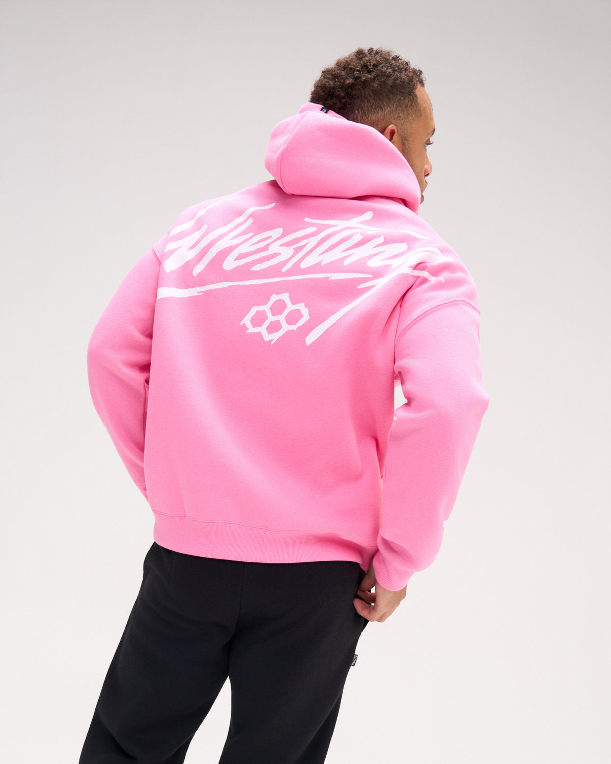 Back view of a male model wearing the RUDIS Art of Wrestling Relaxed Comfort Fleece Hoodie in Bubble Gum Pink, highlighting the oversized white Wrestling script graphic and RUDIS emblem.