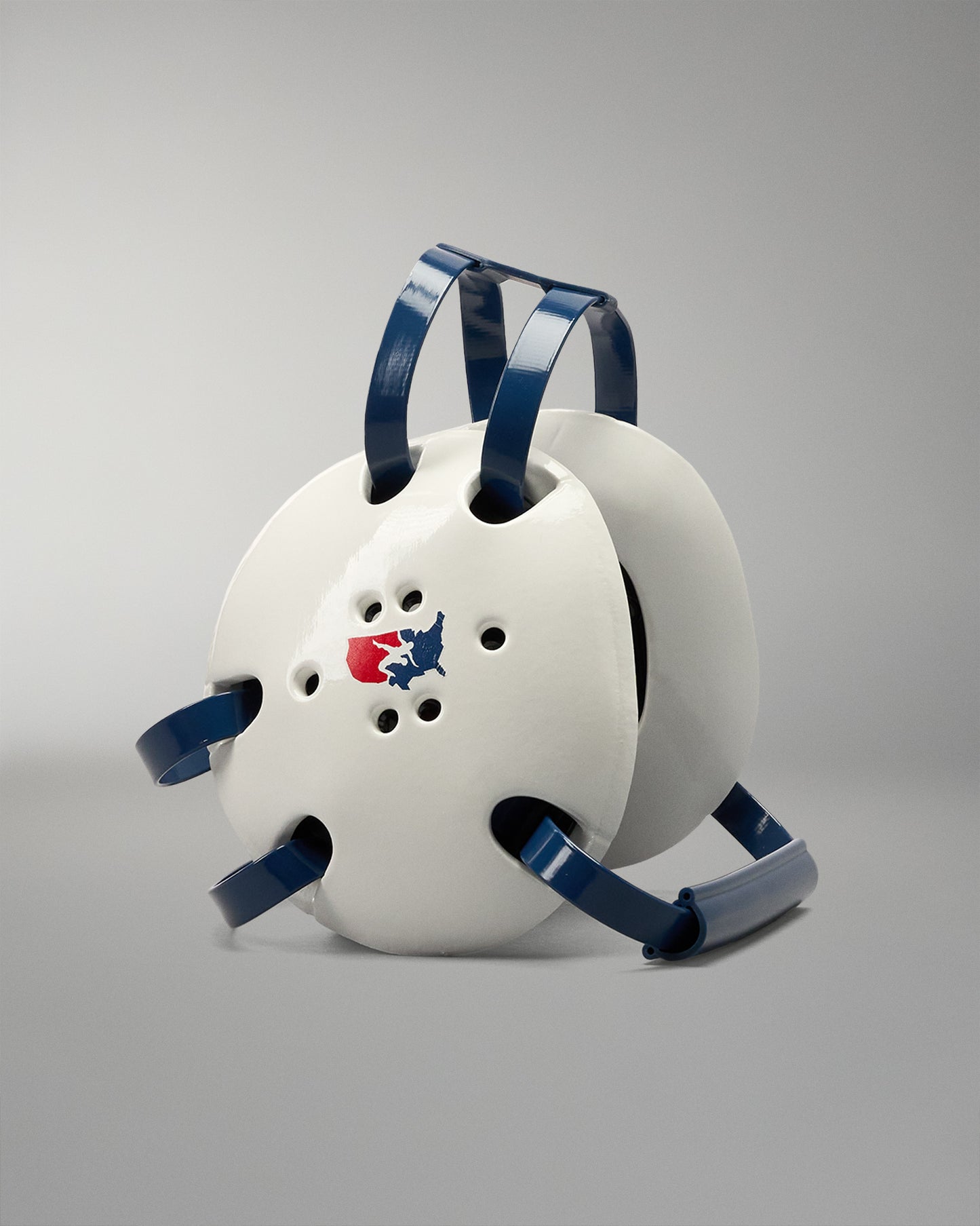 White protective wrestling headgear with blue straps on a gradient blue background. USA Wrestling logo on the headgear side