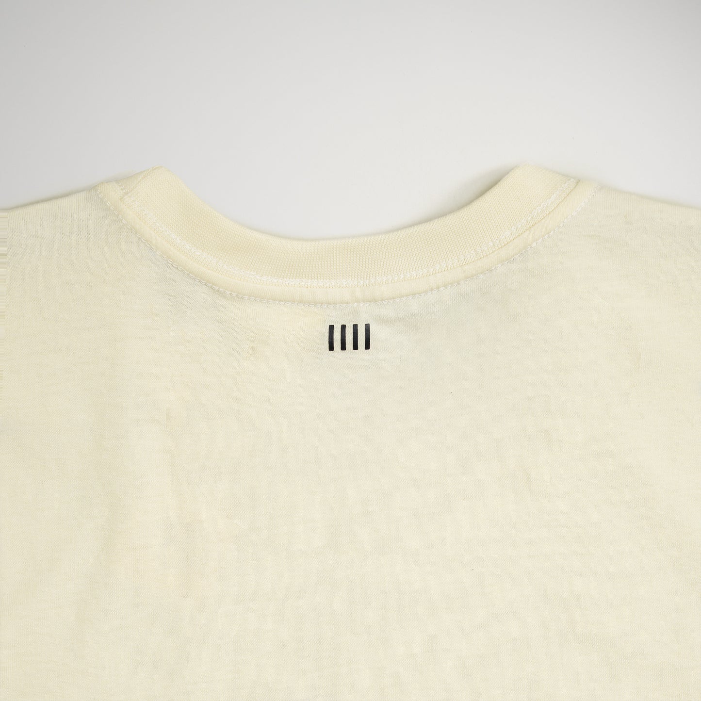 A plain cream-colored t-shirt featuring a subtle minimalistic design element on the back neckline