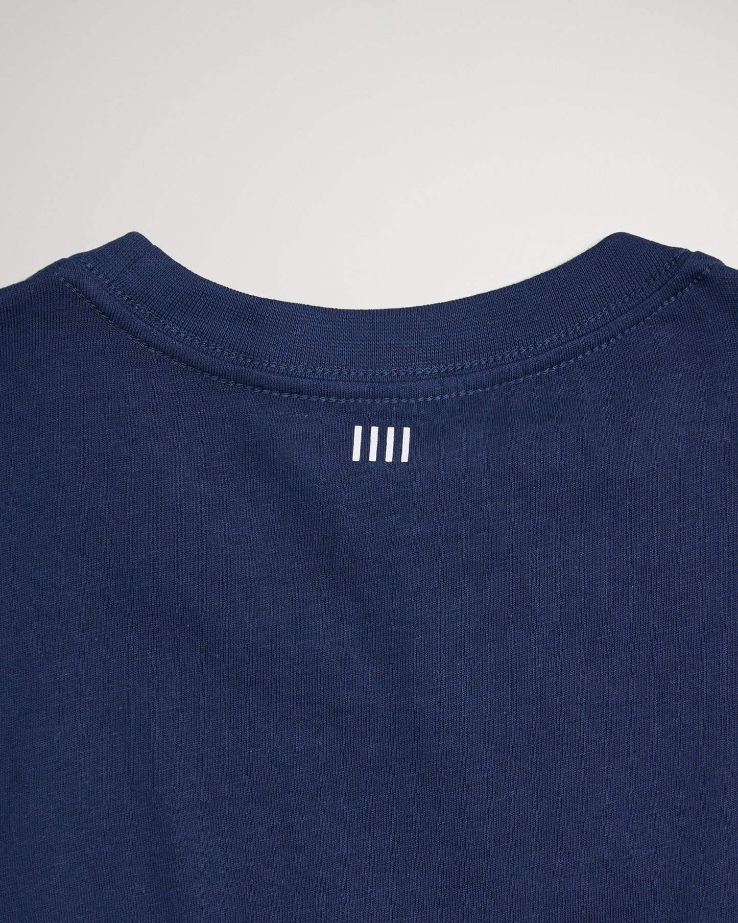 The back neckline of a navy blue t-shirt featuring a minimalist white logo with three horizontal stripes