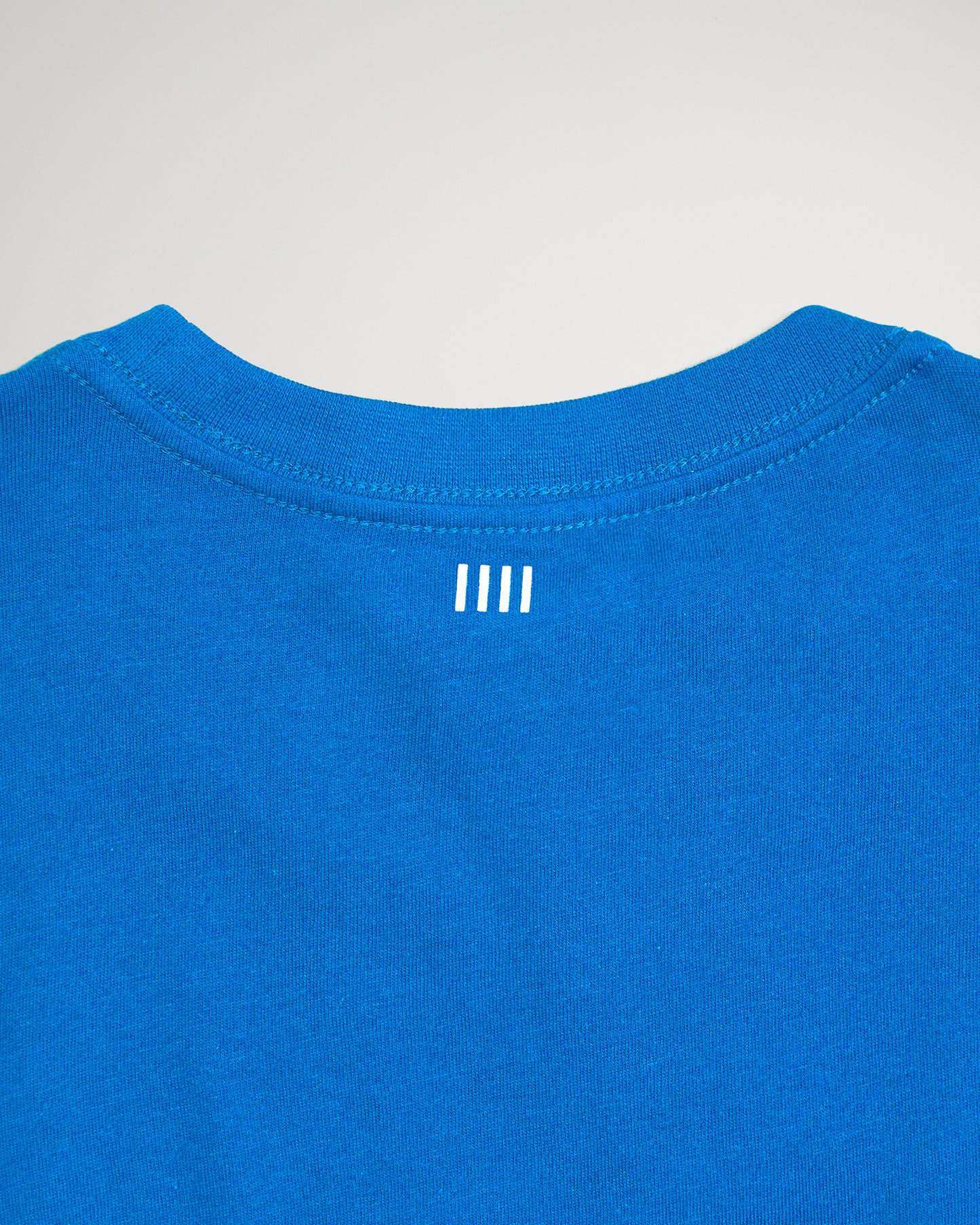 The image features the back of a vibrant blue t-shirt highlighting a minimalist design with three vertical white stripes near the neckline