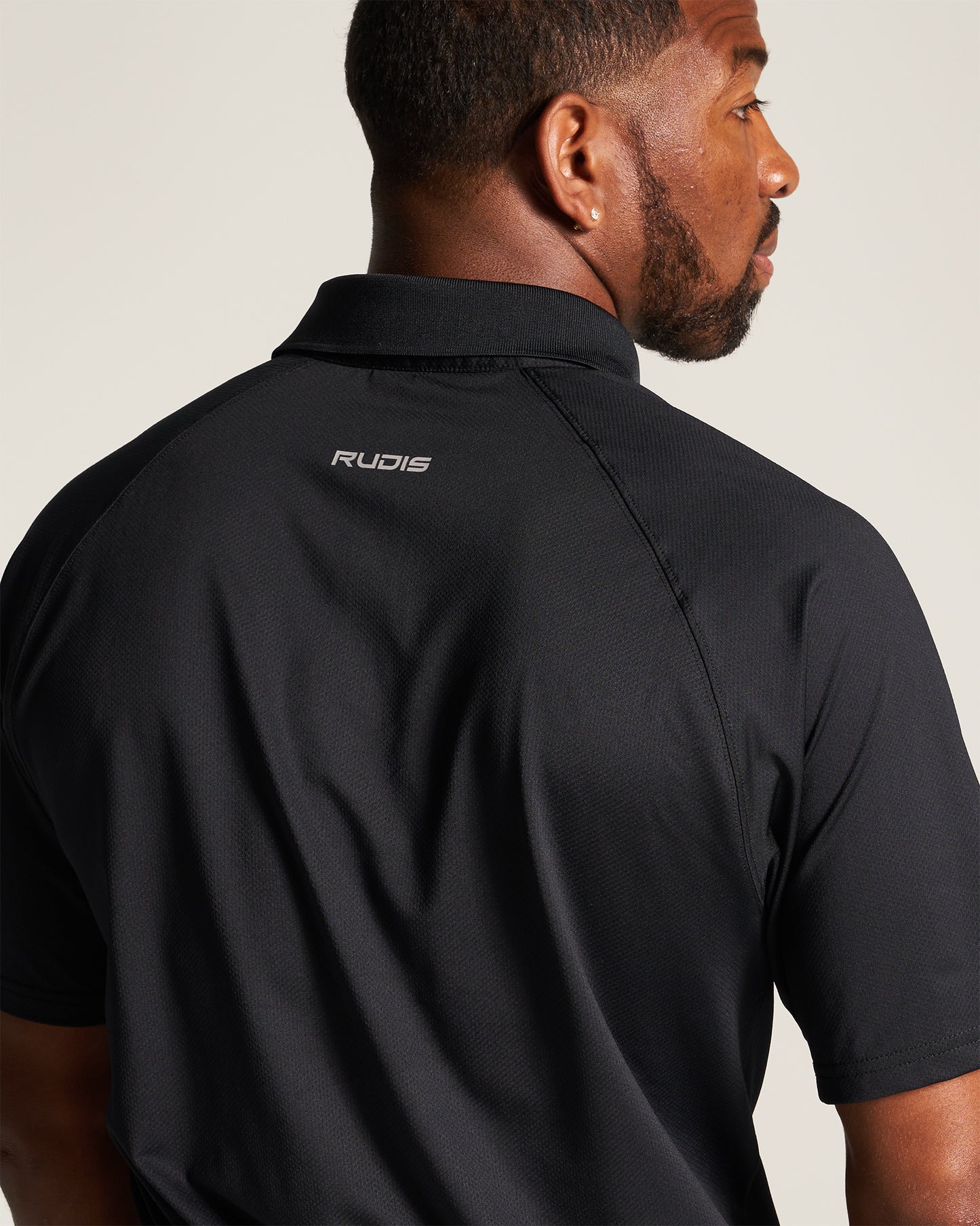 A close-up view of a man wearing a black athletic shirt with the RUDIS logo prominently displayed on the back