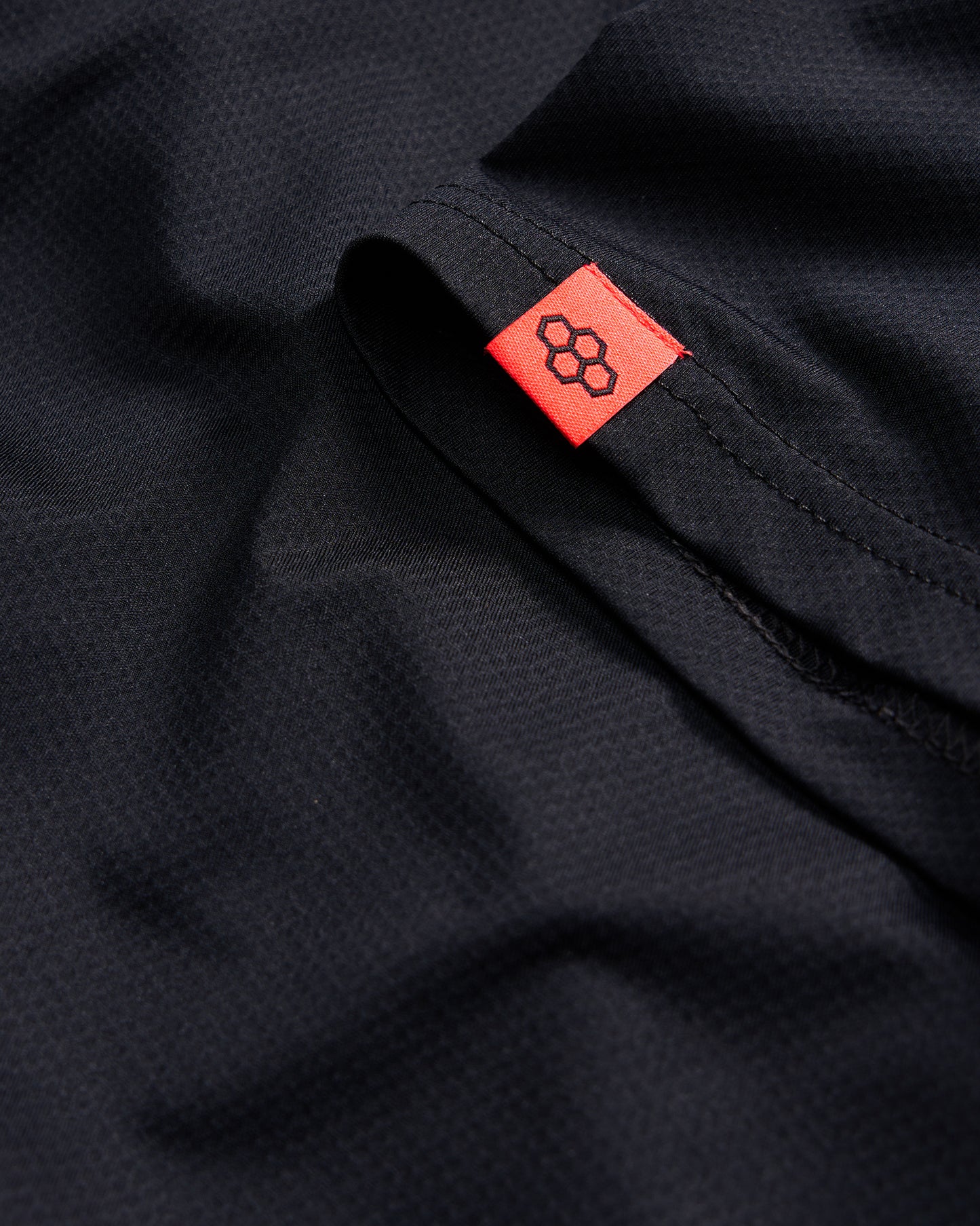 A close-up of a black fabric showcasing a textured surface with a bright red tag featuring a logo on the edge
