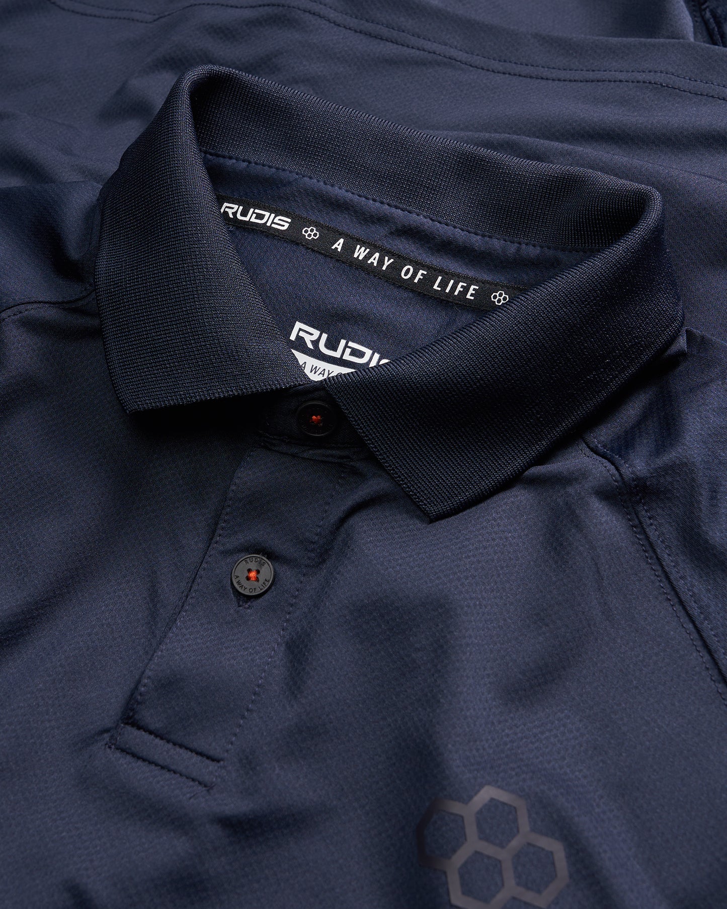 A close-up view of a navy blue polo shirt featuring the brand name RUDIS and the slogan A WAY OF LIFE inside the collar